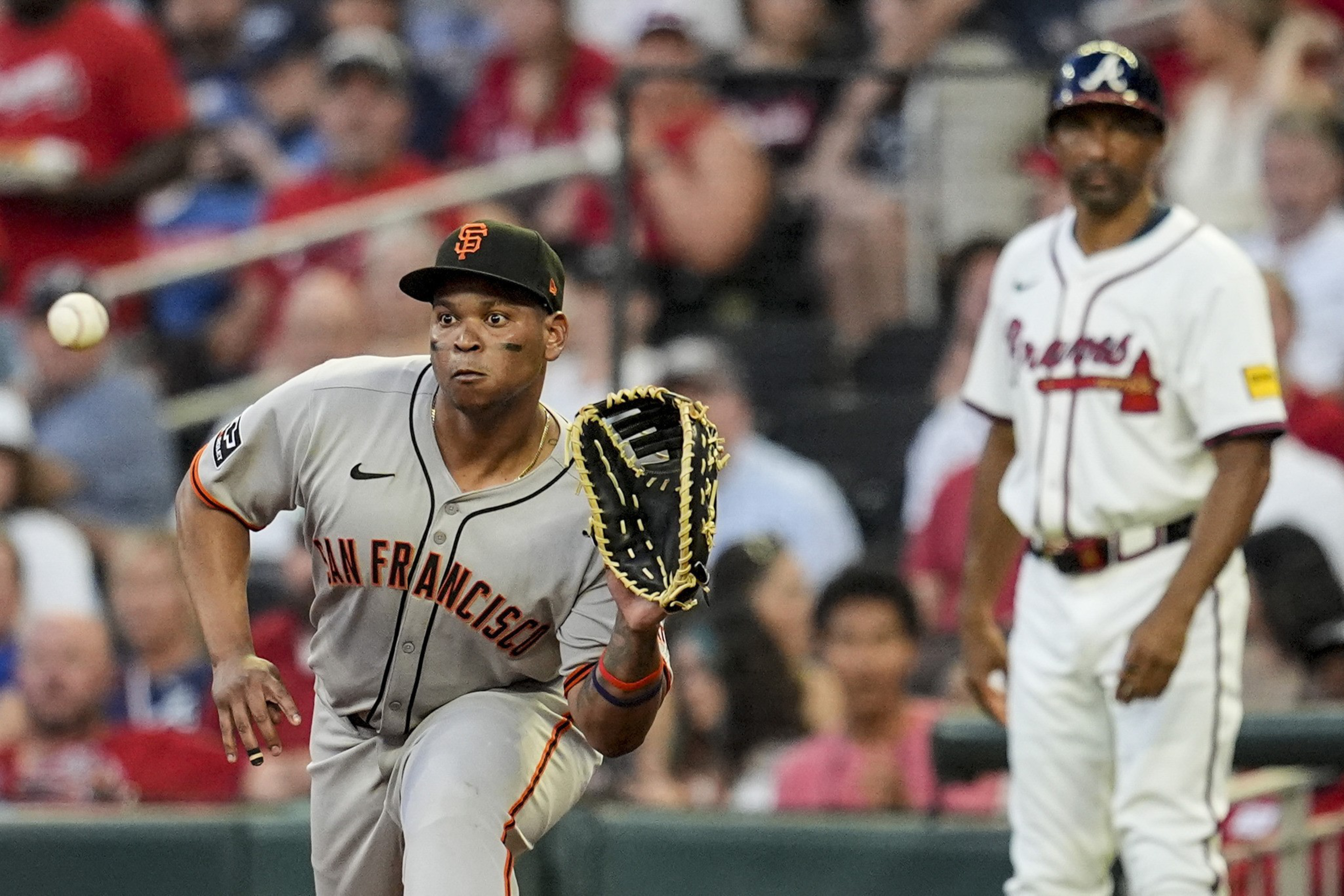 A baseball player in a San Francisco jersey focuses intently with a glove ready to catch as another player in a Braves uniform stands in the background.