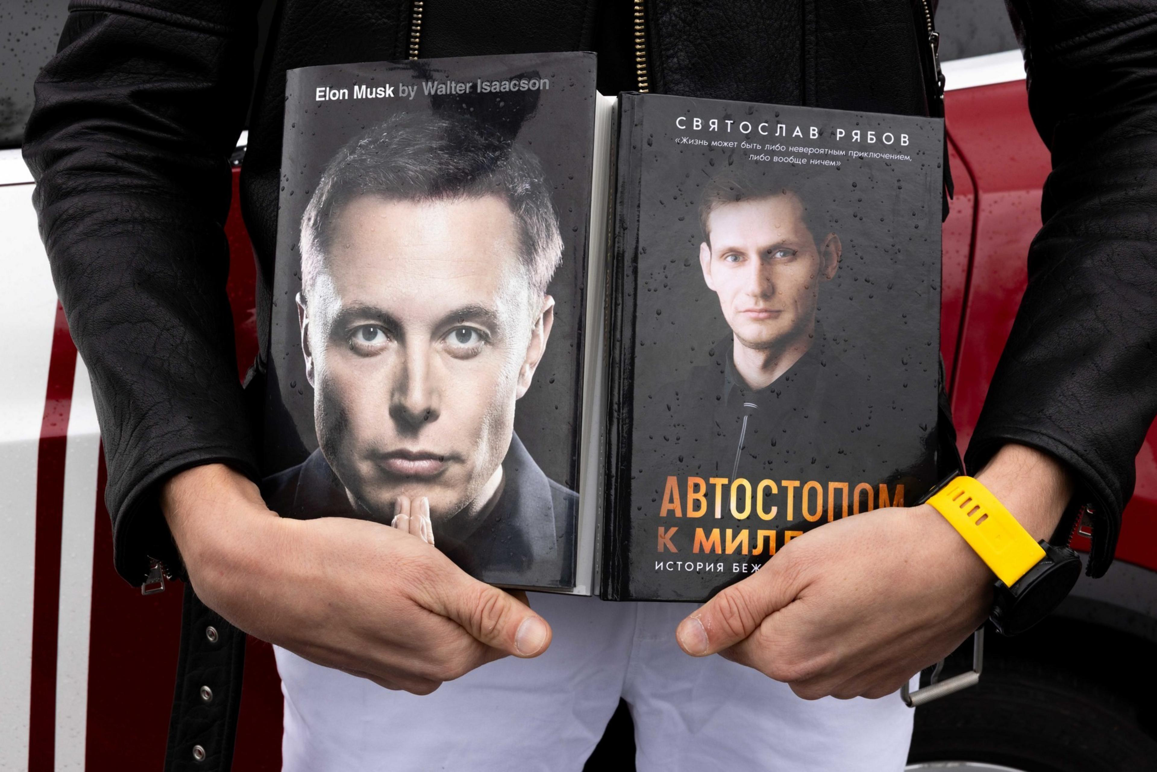 A person is holding two books with portraits on their covers. The left book features a man in a suit and the right book has text in a different language.