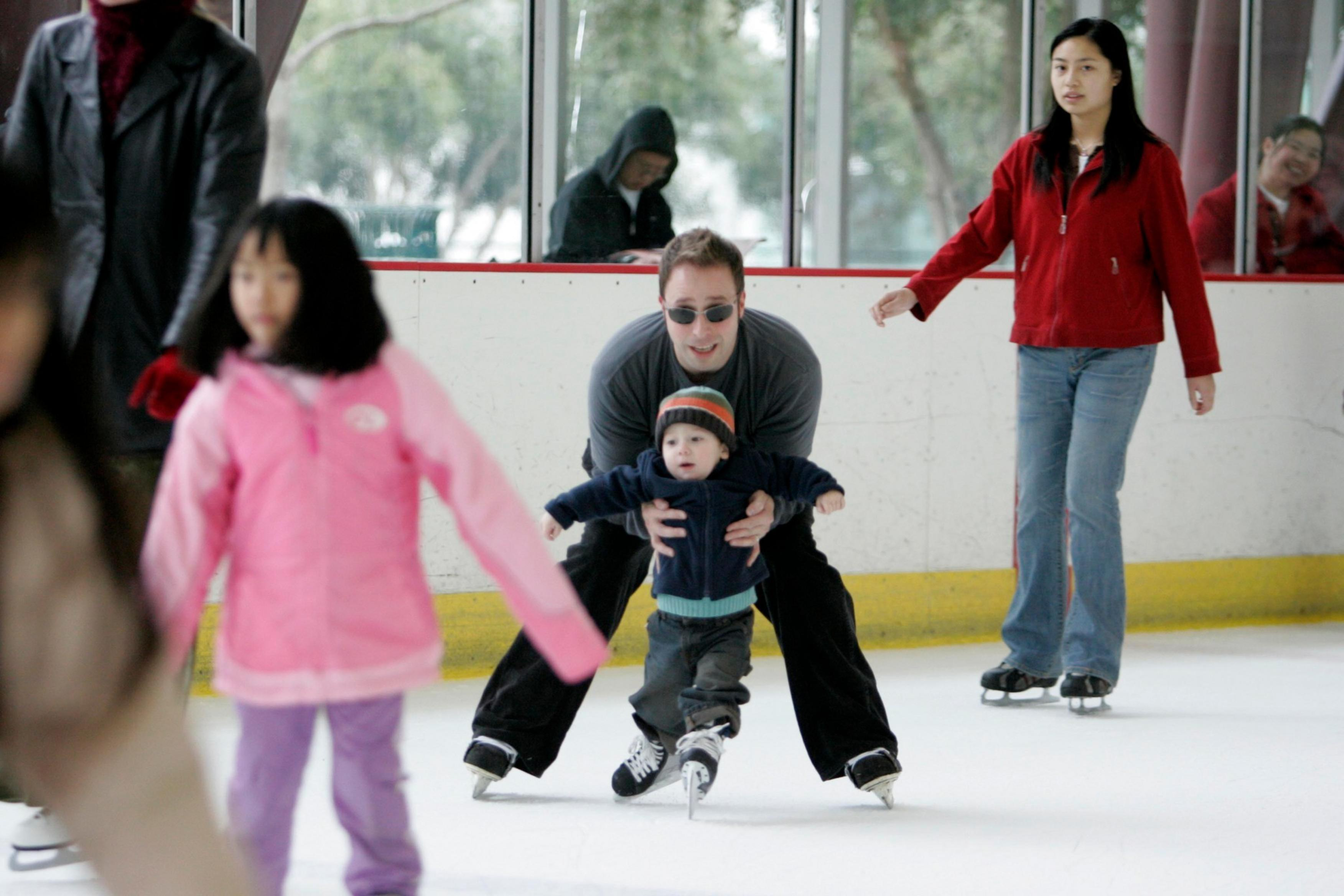Toddler learns to ice skate with help.