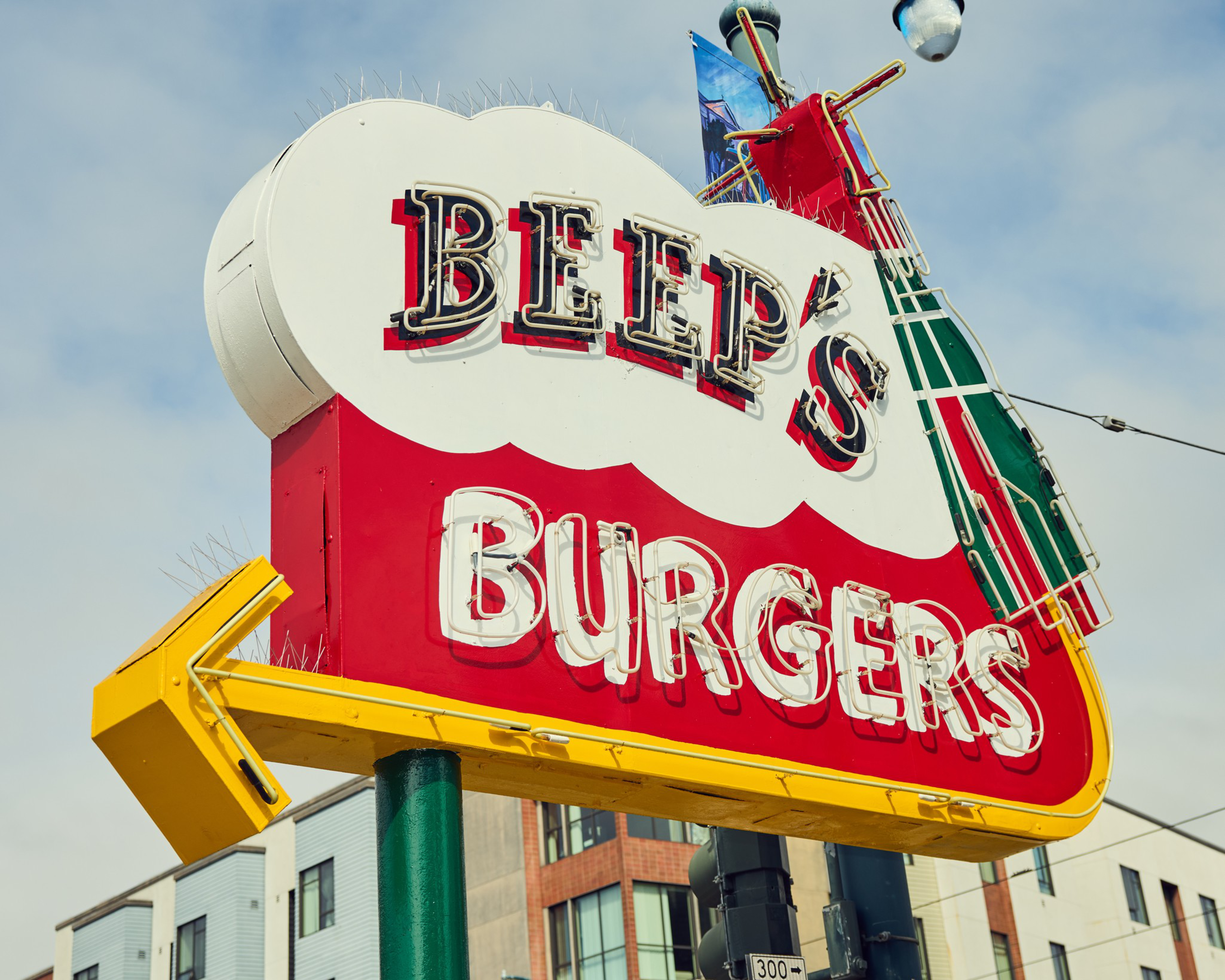 The image shows a retro-style sign for &quot;Beep's Burgers&quot; with neon letters on a red and white background, featuring a yellow arrow pointing left.