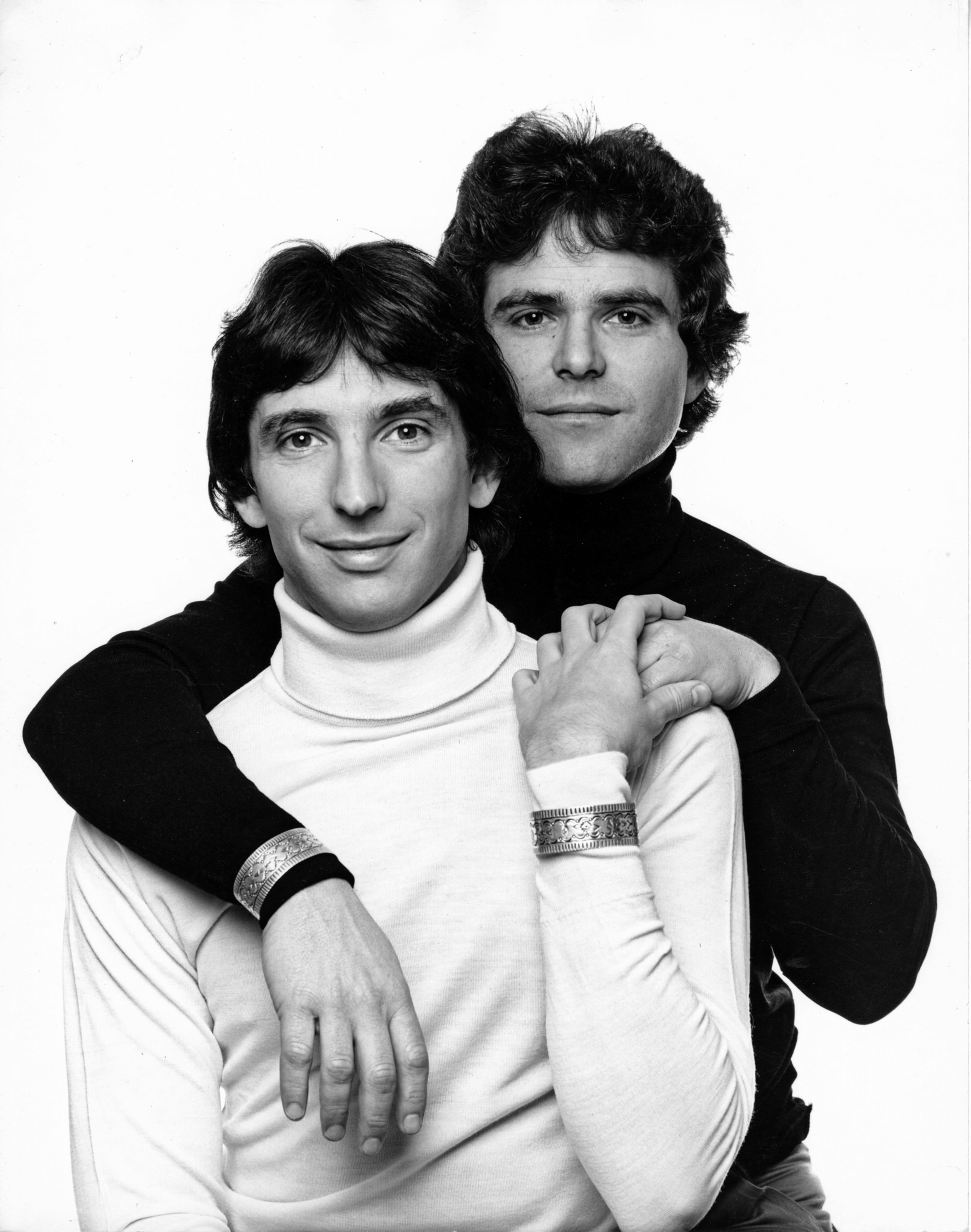 Two men pose closely, one in a black turtleneck behind the other in a ...