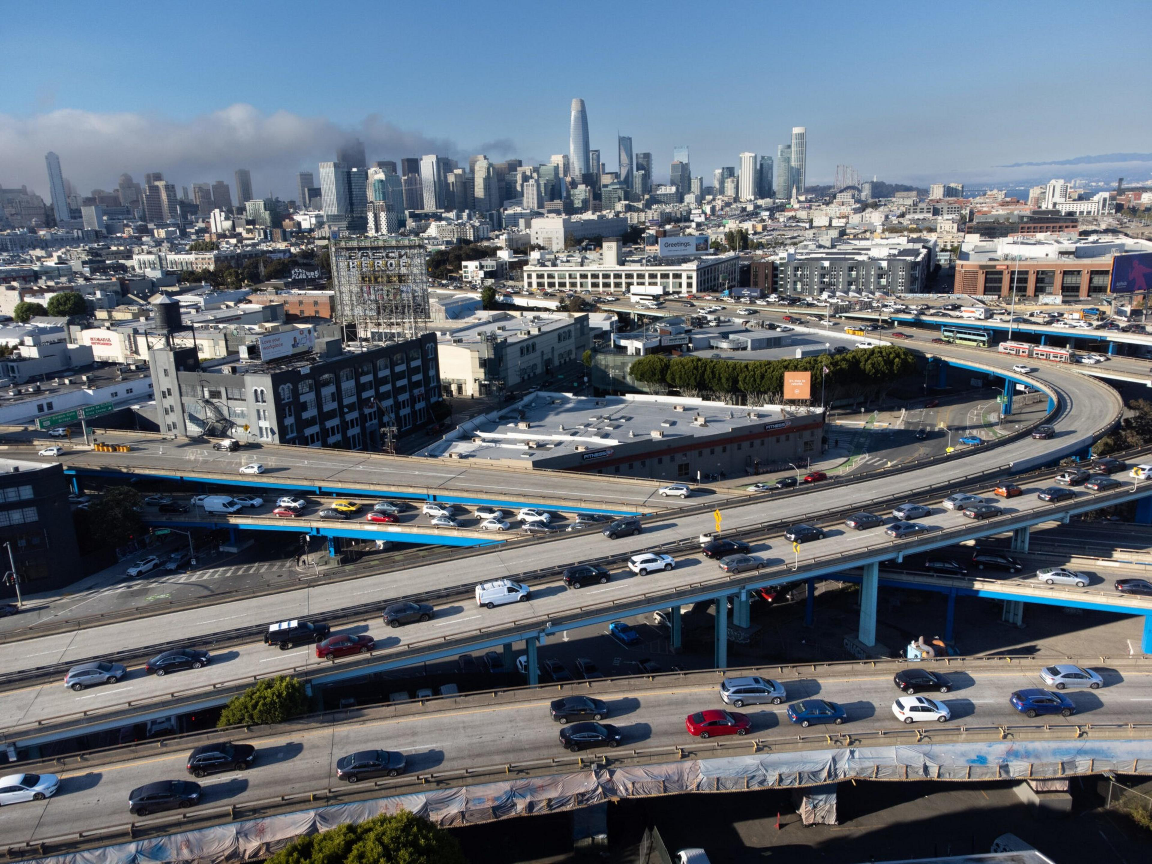 Aerial view of a cityscape with busy multilane highways and a backdrop of skyscrapers under a clear sky.