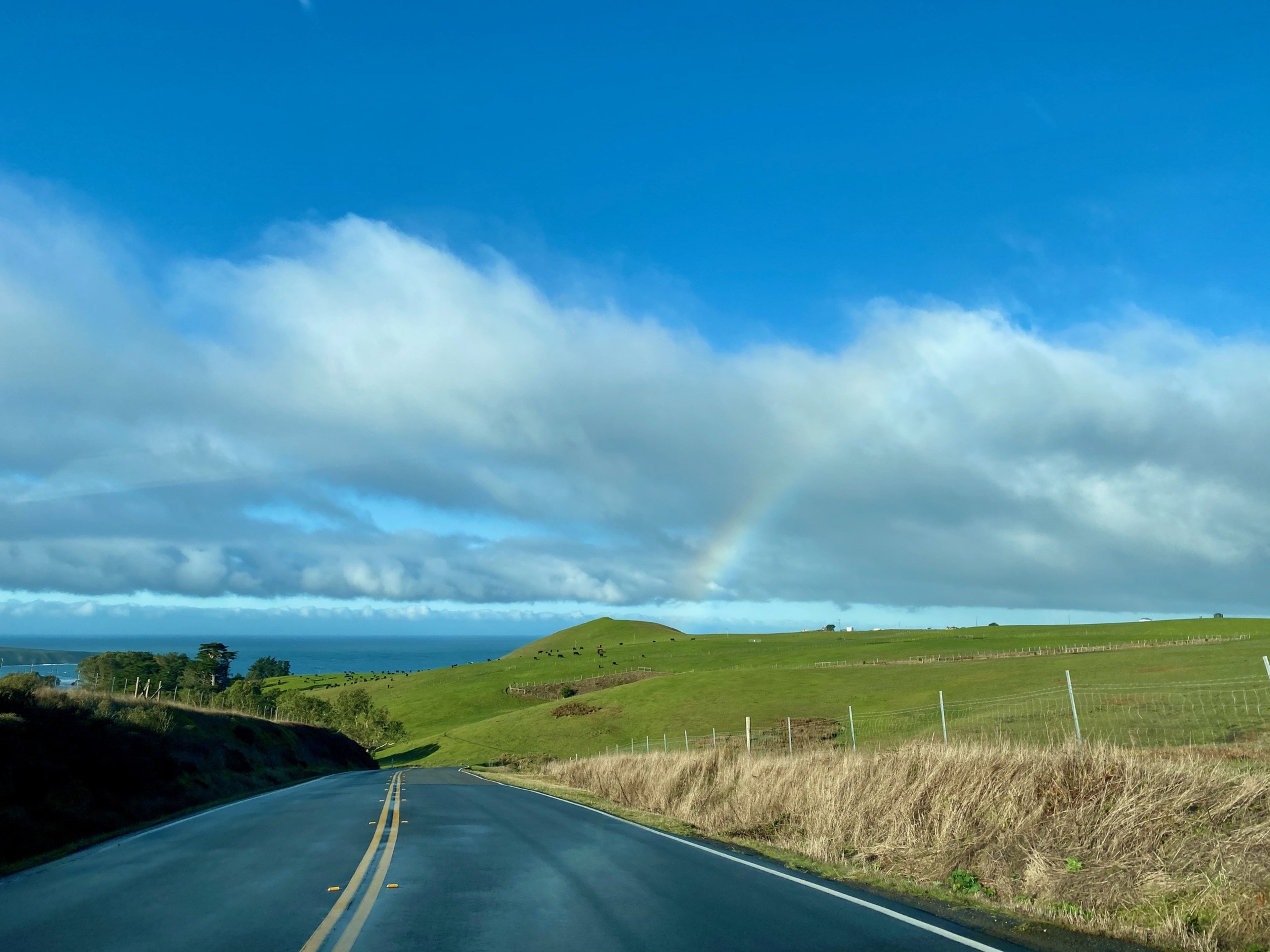 A highway with fields next to it under a blue sky with a few clouds. 