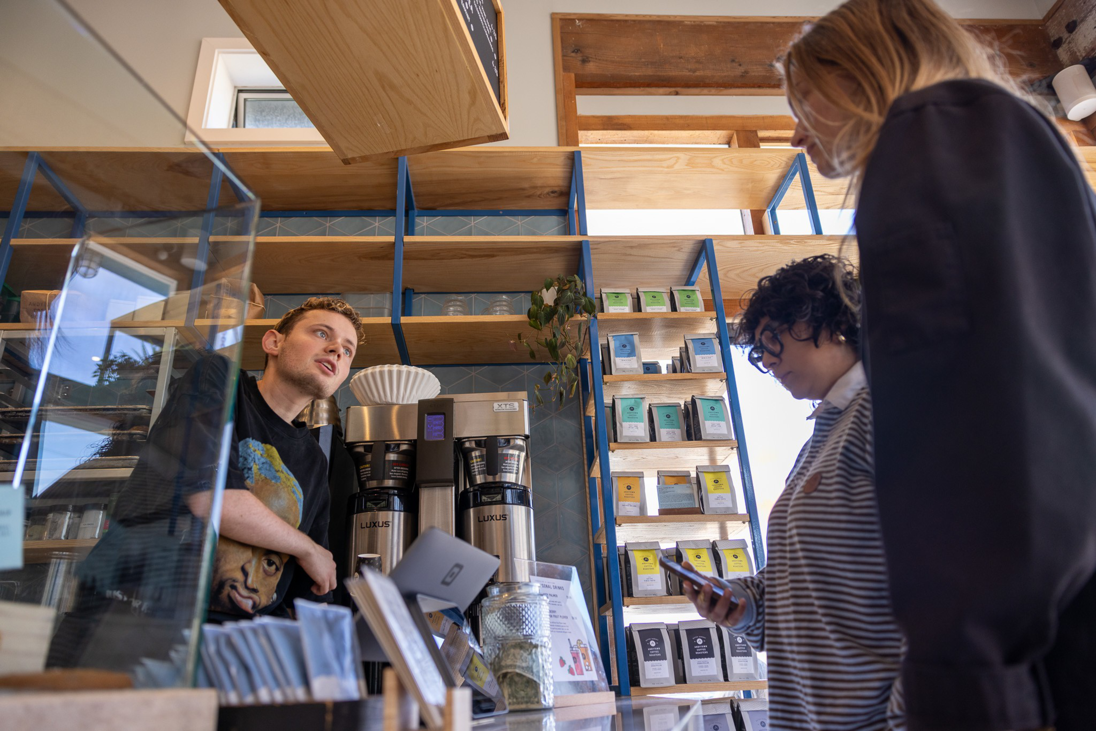 A male barista serves two female customers at a coffee shop.