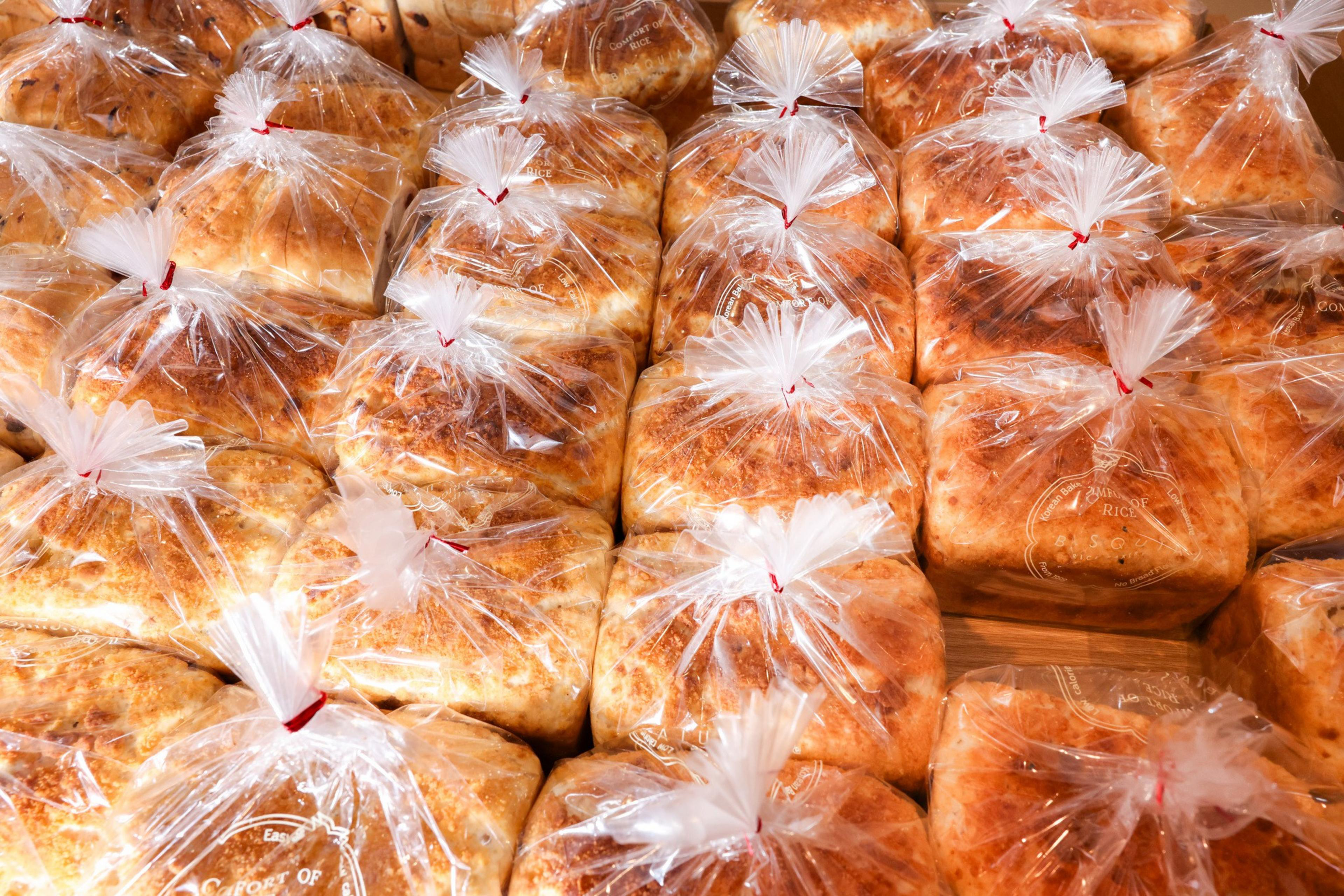 The image shows several loaves of bread individually wrapped in clear plastic bags with twist ties. The bread appears golden brown and is displayed neatly.