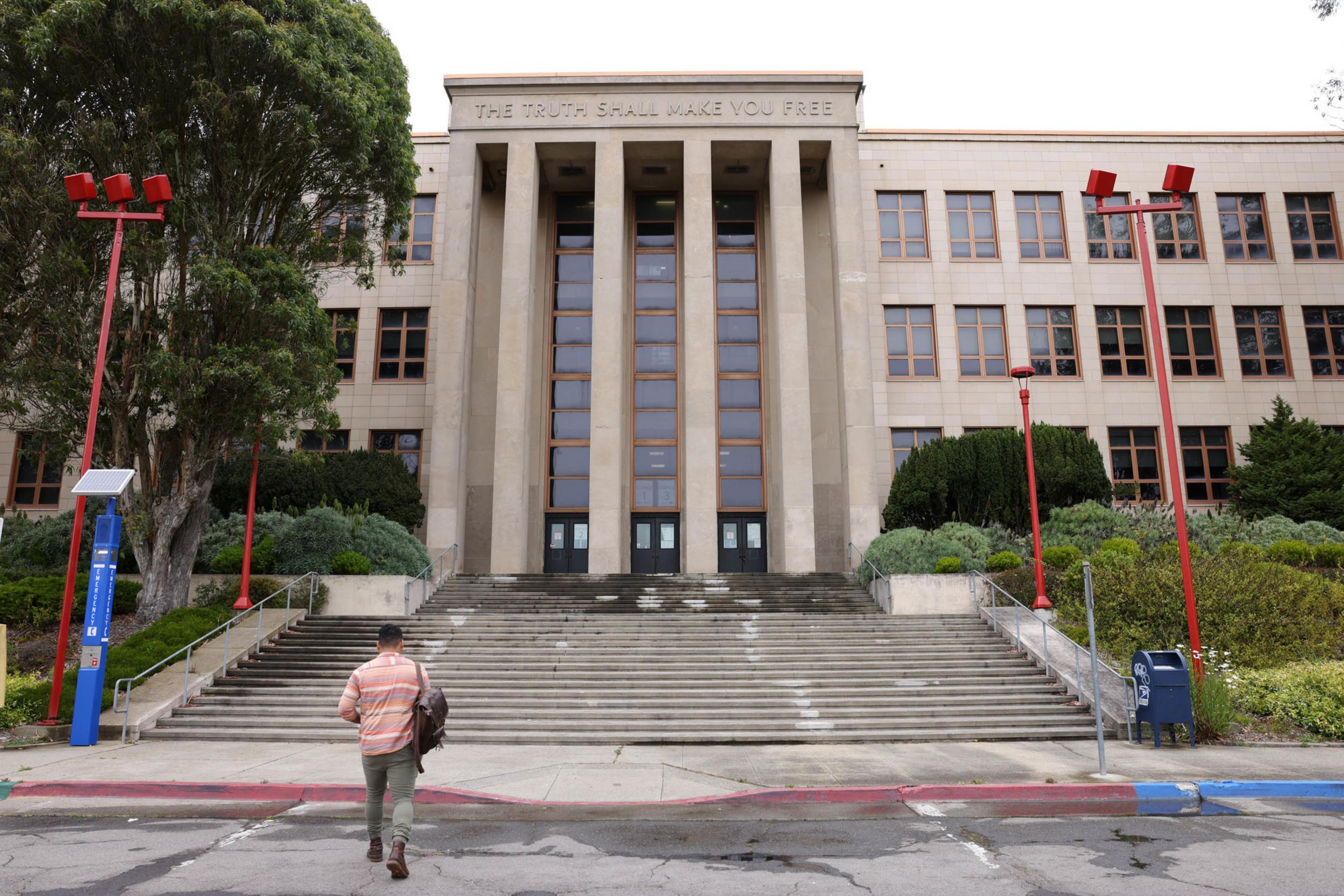 A person walks up wide steps toward a large building with tall columns and the inscription "THE TRUTH SHALL MAKE YOU FREE" above the entrance.