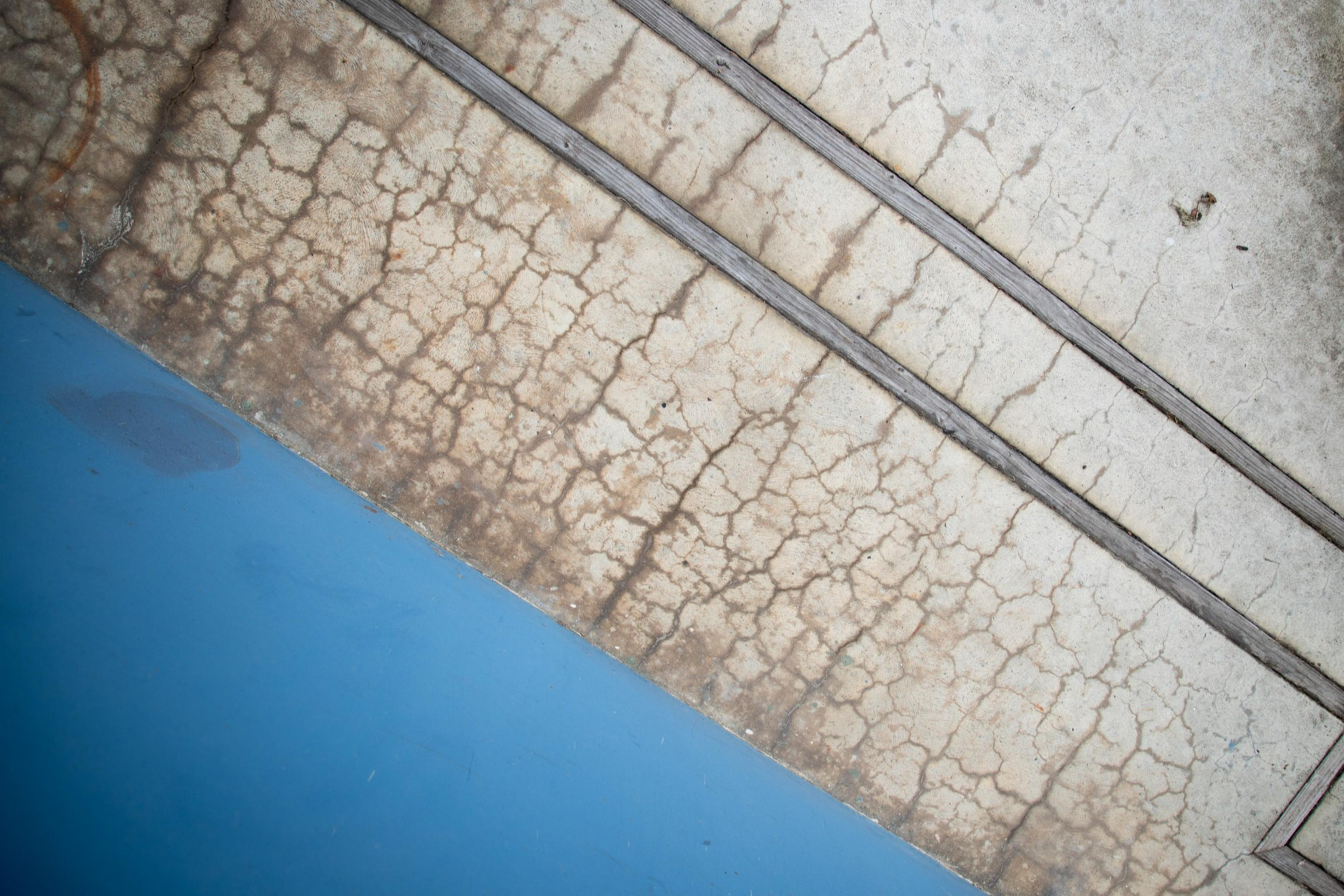 A cracked, weathered concrete surface with two parallel grooves is adjacent to a solid blue area, creating a striking contrast of textures and colors.
