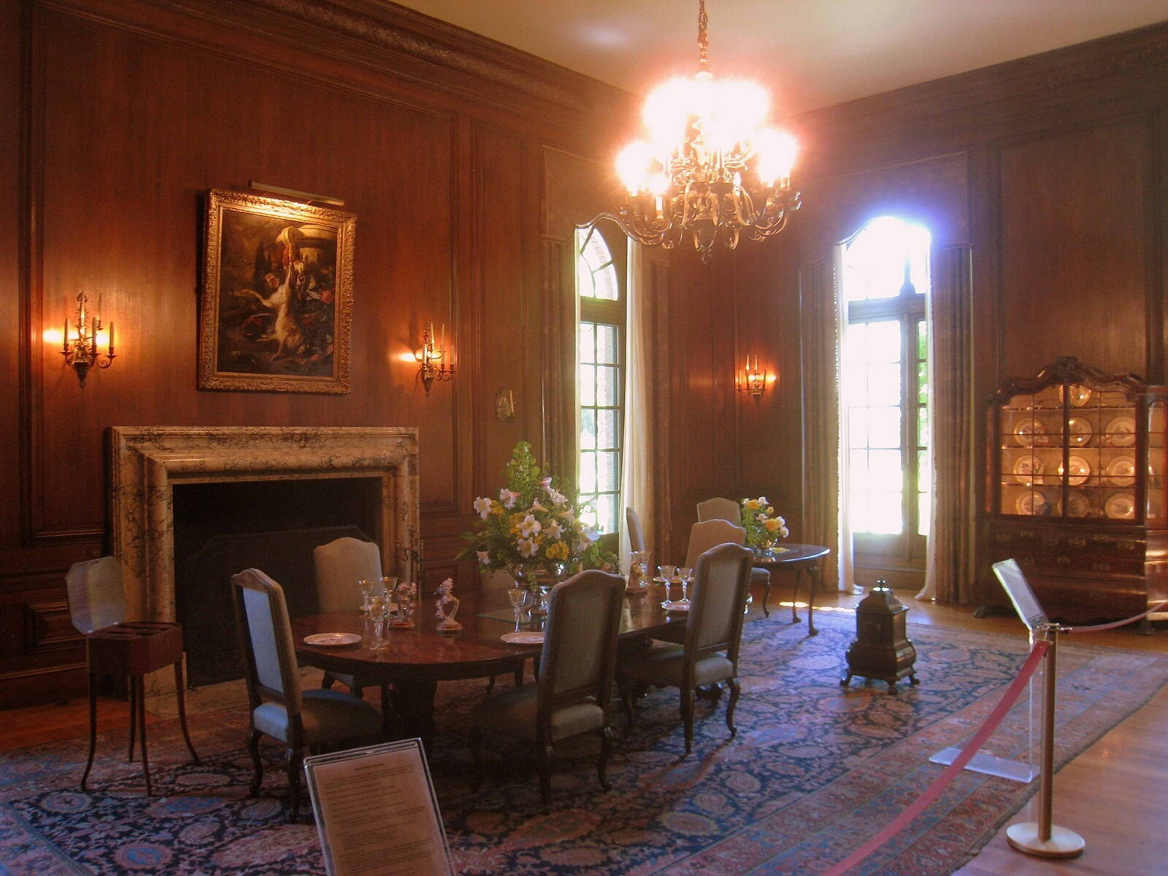 A wood paneled dining room with Victorian era decorations, chandelier, fireplace, etc.