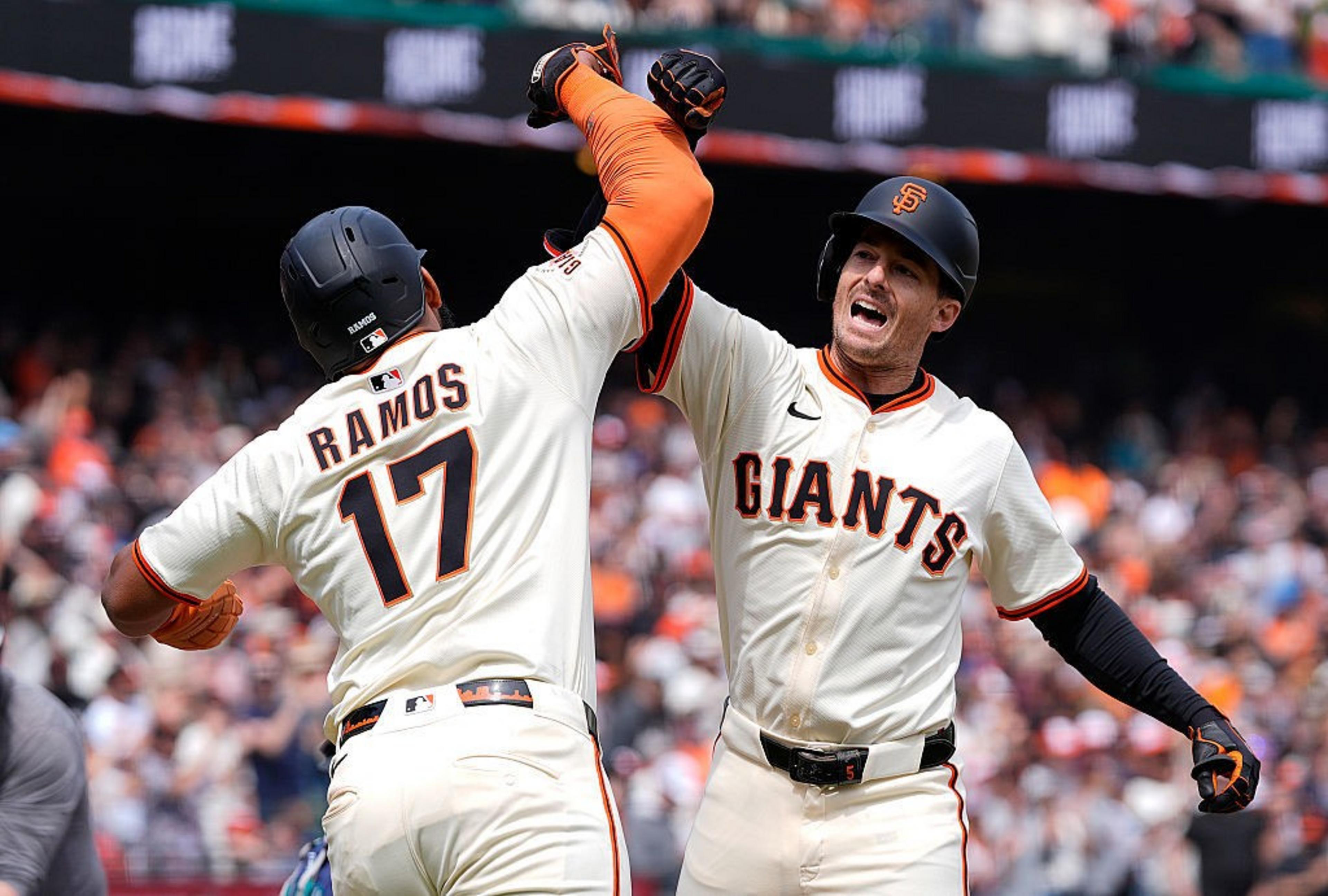 Two baseball players in Giants uniforms celebrate with a high elbow bump on the field, wearing helmets and jerseys with "Giants" and the number 17 visible.