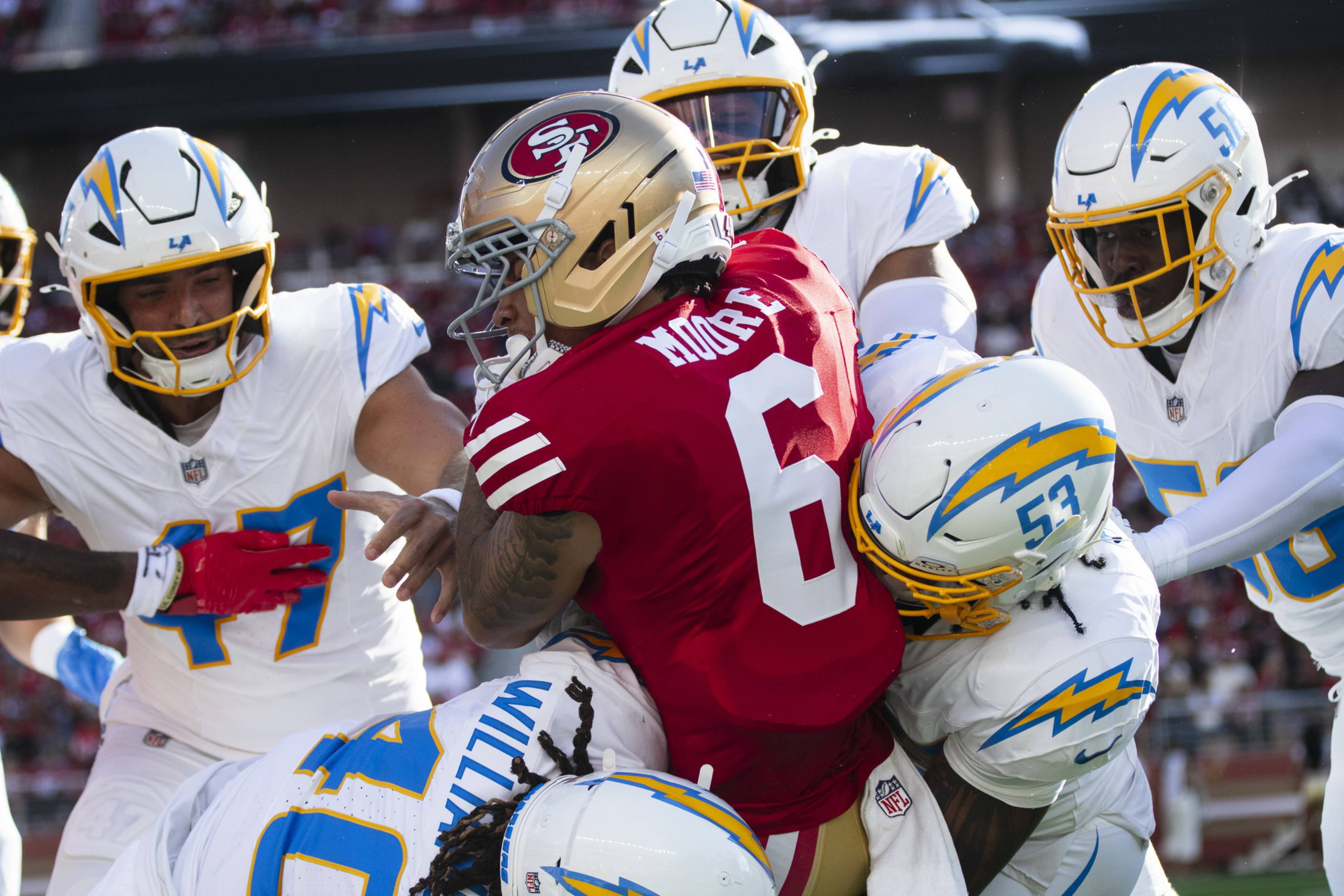 A San Francisco 49ers player wearing number 6 is tackled by four Los Angeles Chargers players during a football game.