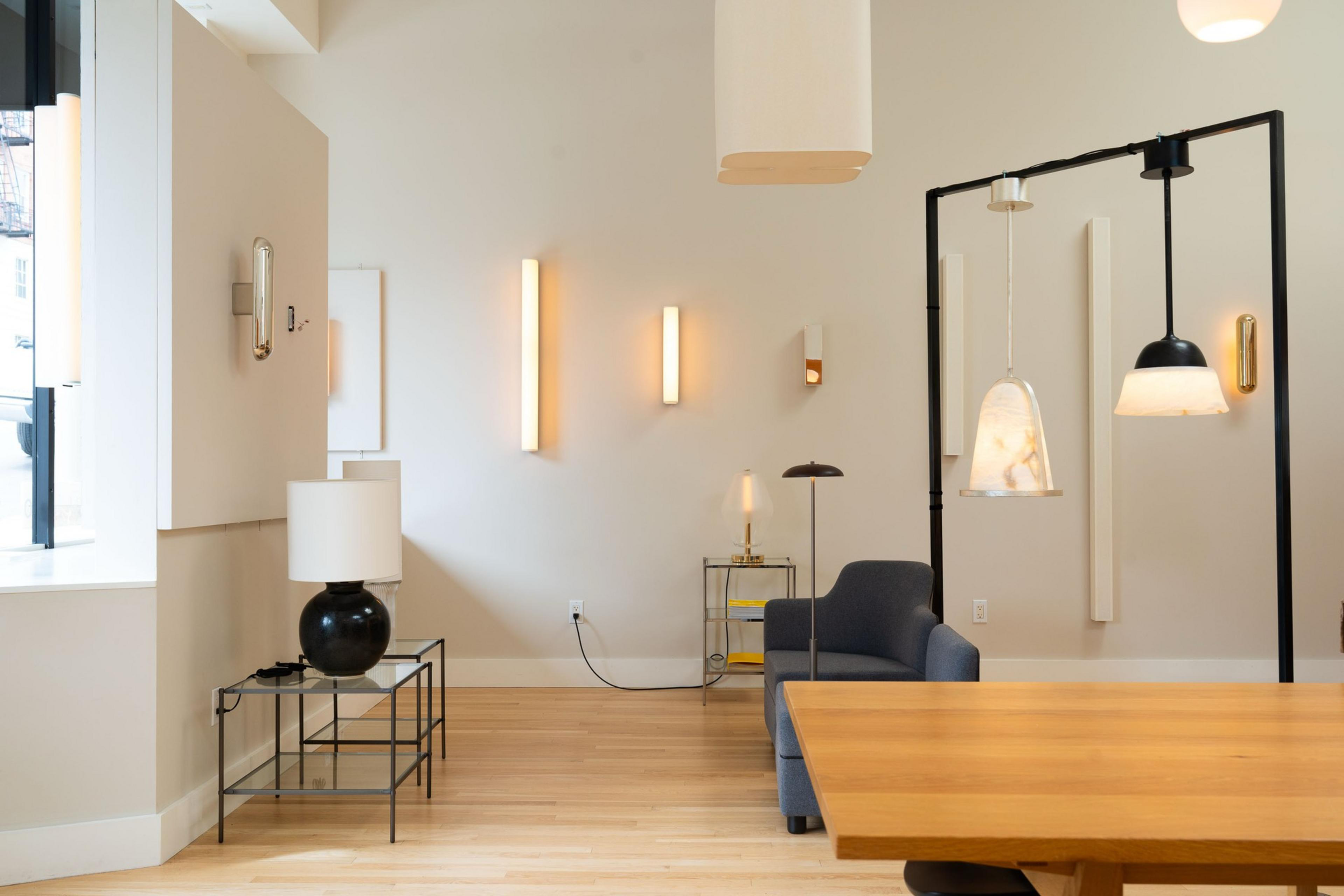 The image shows a modern room with wooden floors, various wall and pendant lights, a dark blue armchair, a glass-top side table, and a wooden dining table.