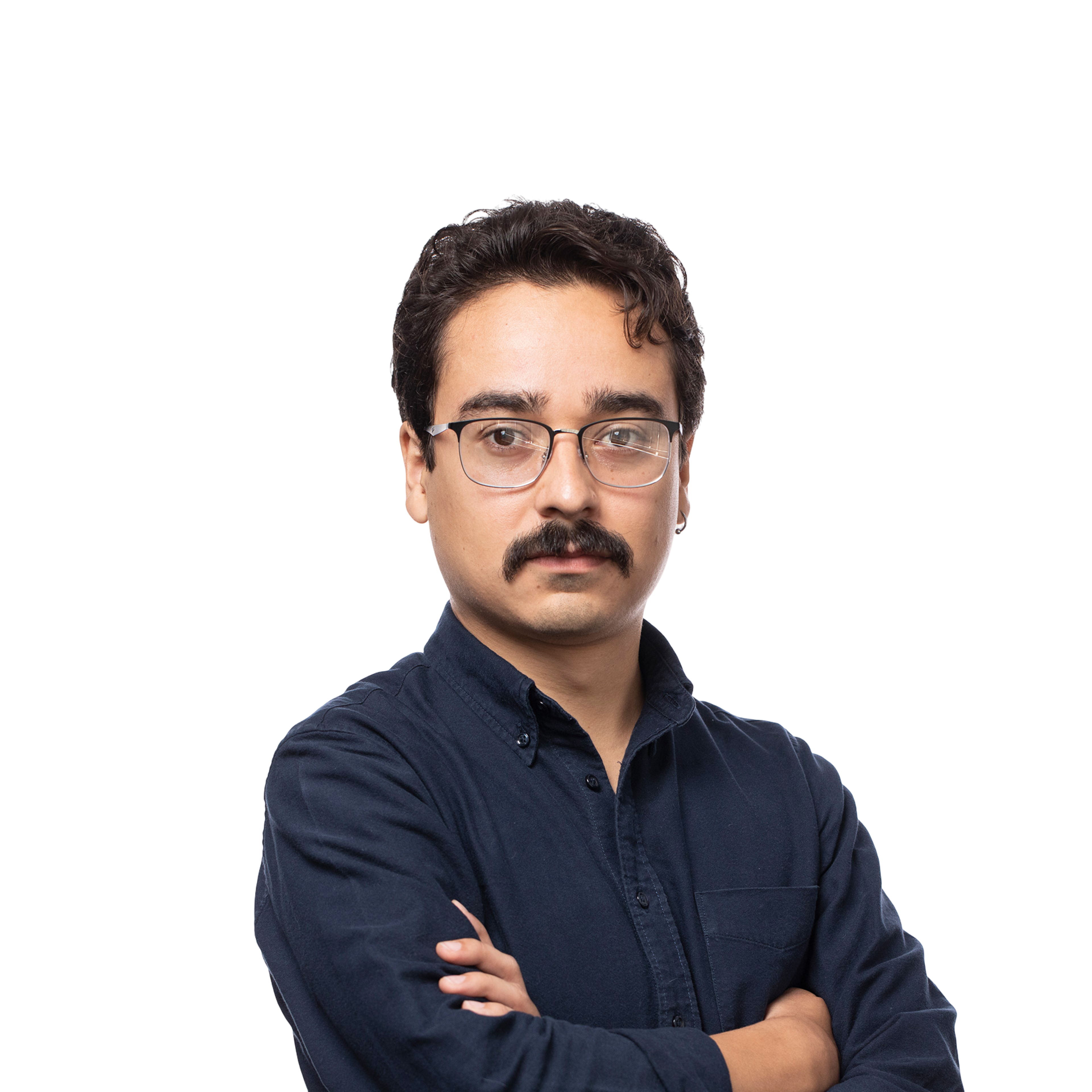 A man with curly dark hair, a mustache, and glasses wears a dark blue button-up shirt with arms crossed, looking directly forward.