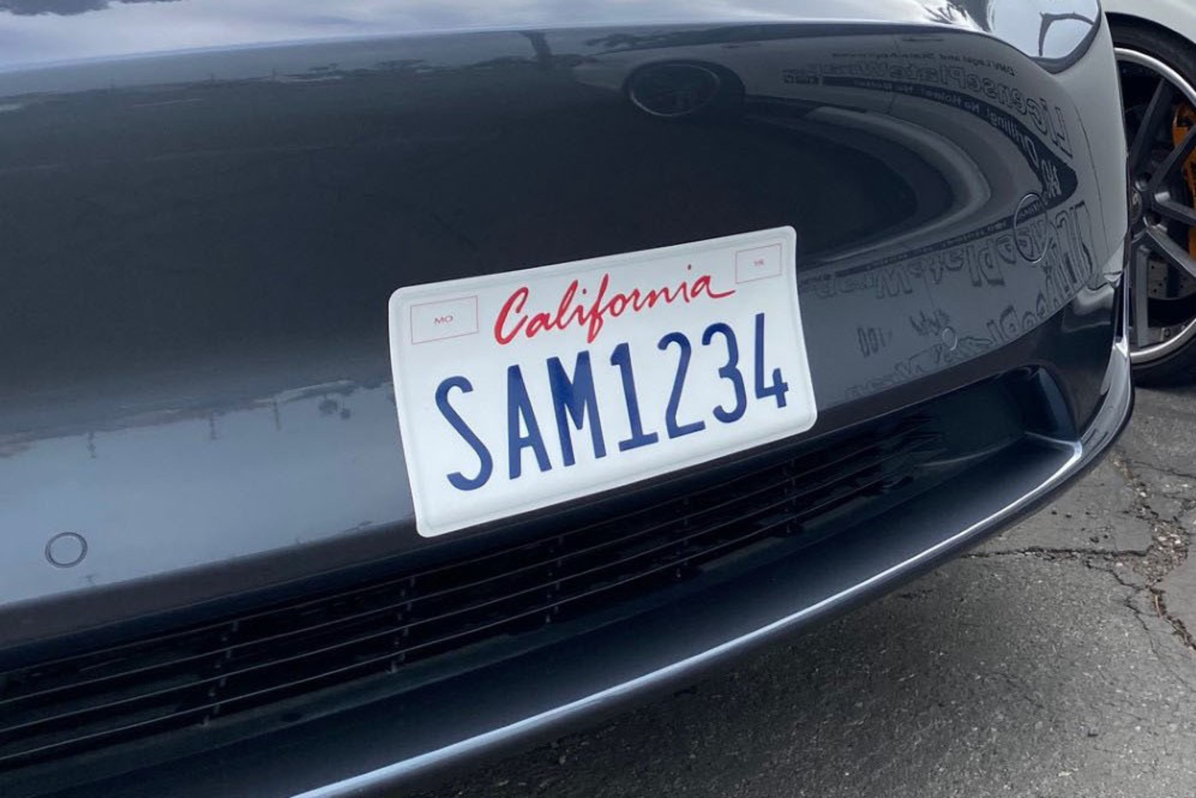A wrapped sticker license plate adhered to front bumper on a vehicle with a California license plate.