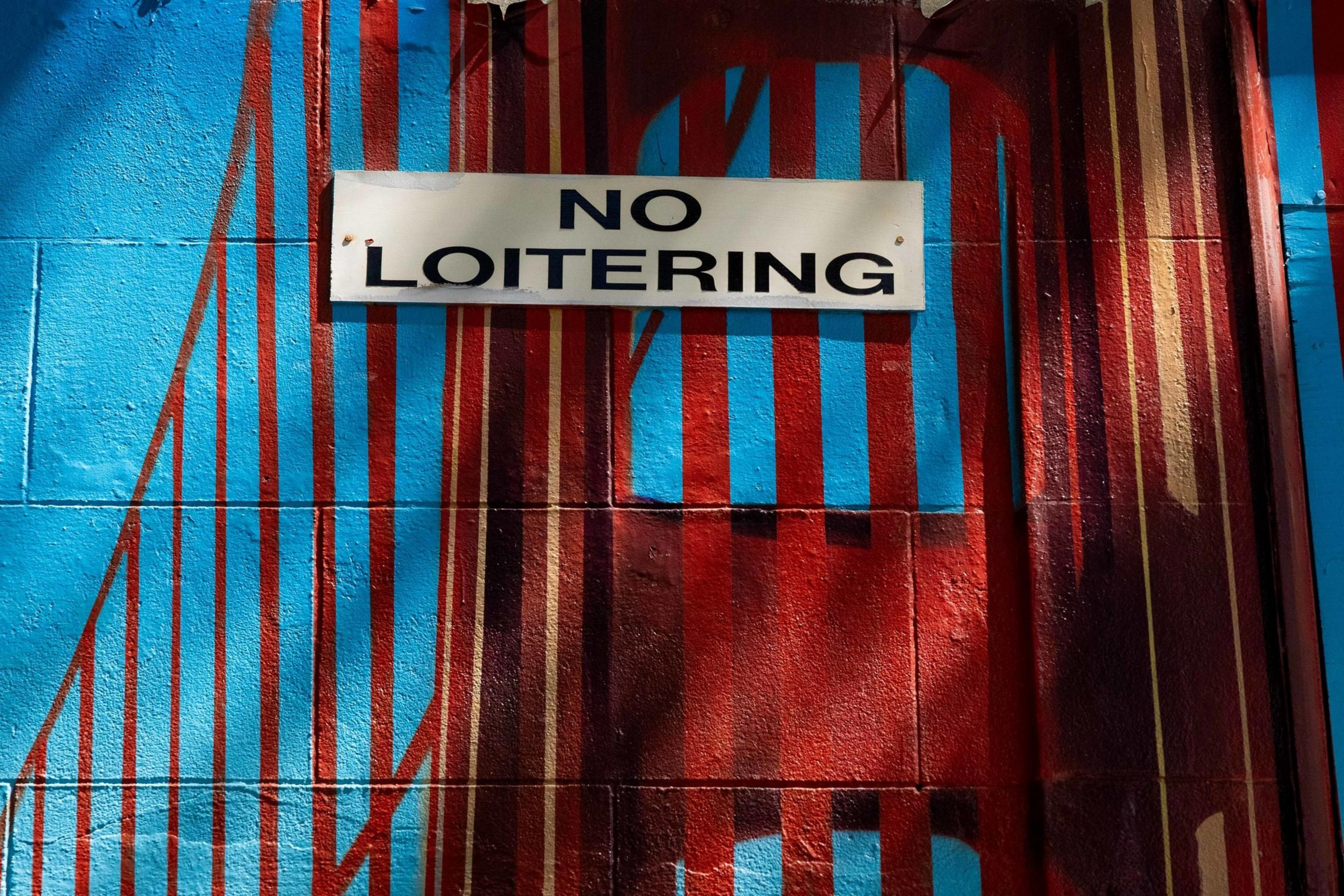 A &quot;No Loitering&quot; sign is displayed on a wall with bold blue and red vertical stripes, creating a vivid and colorful background.