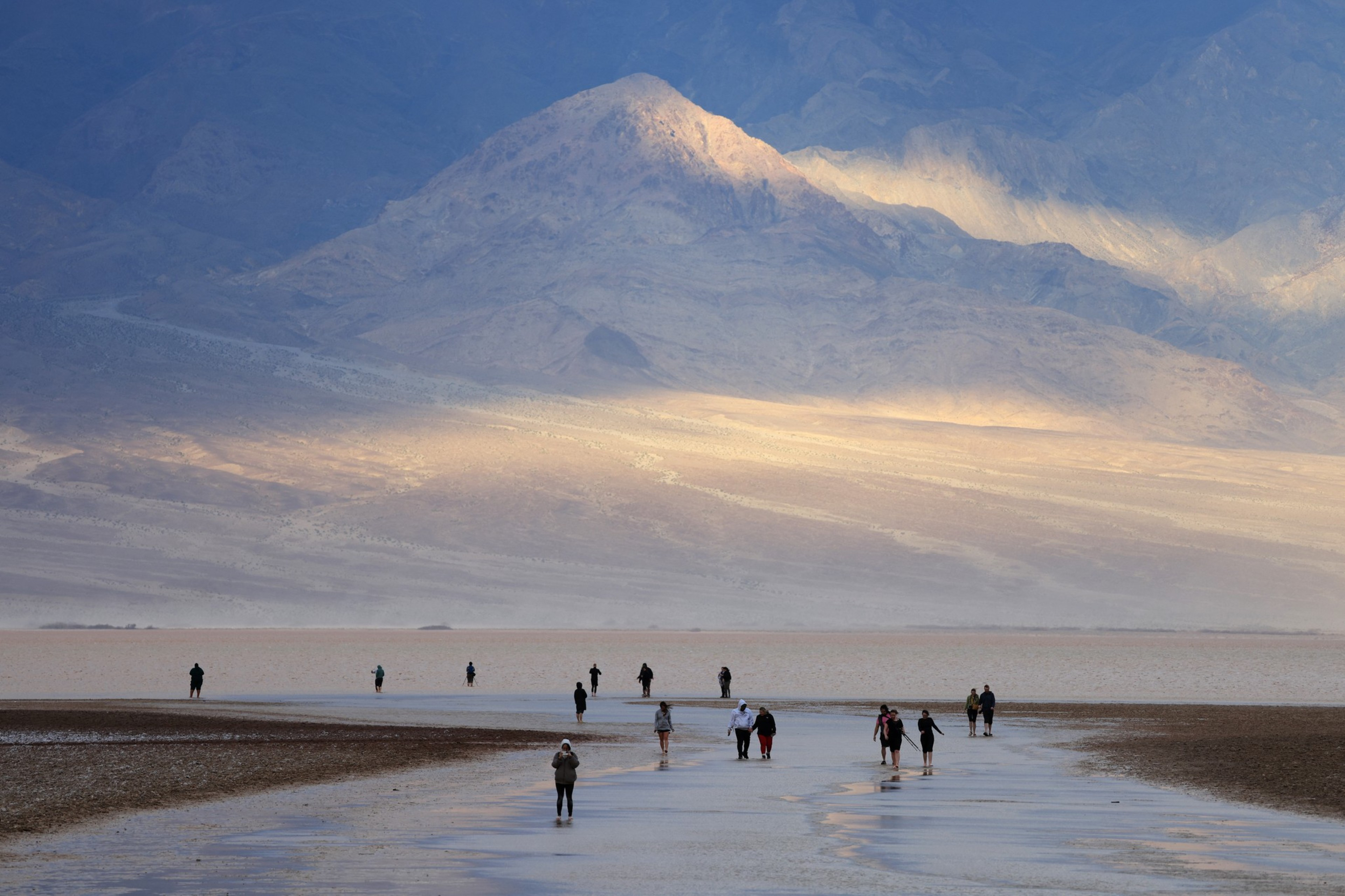 a shallow lake at dusk with distant people in it, with a ghostly mountain beyond