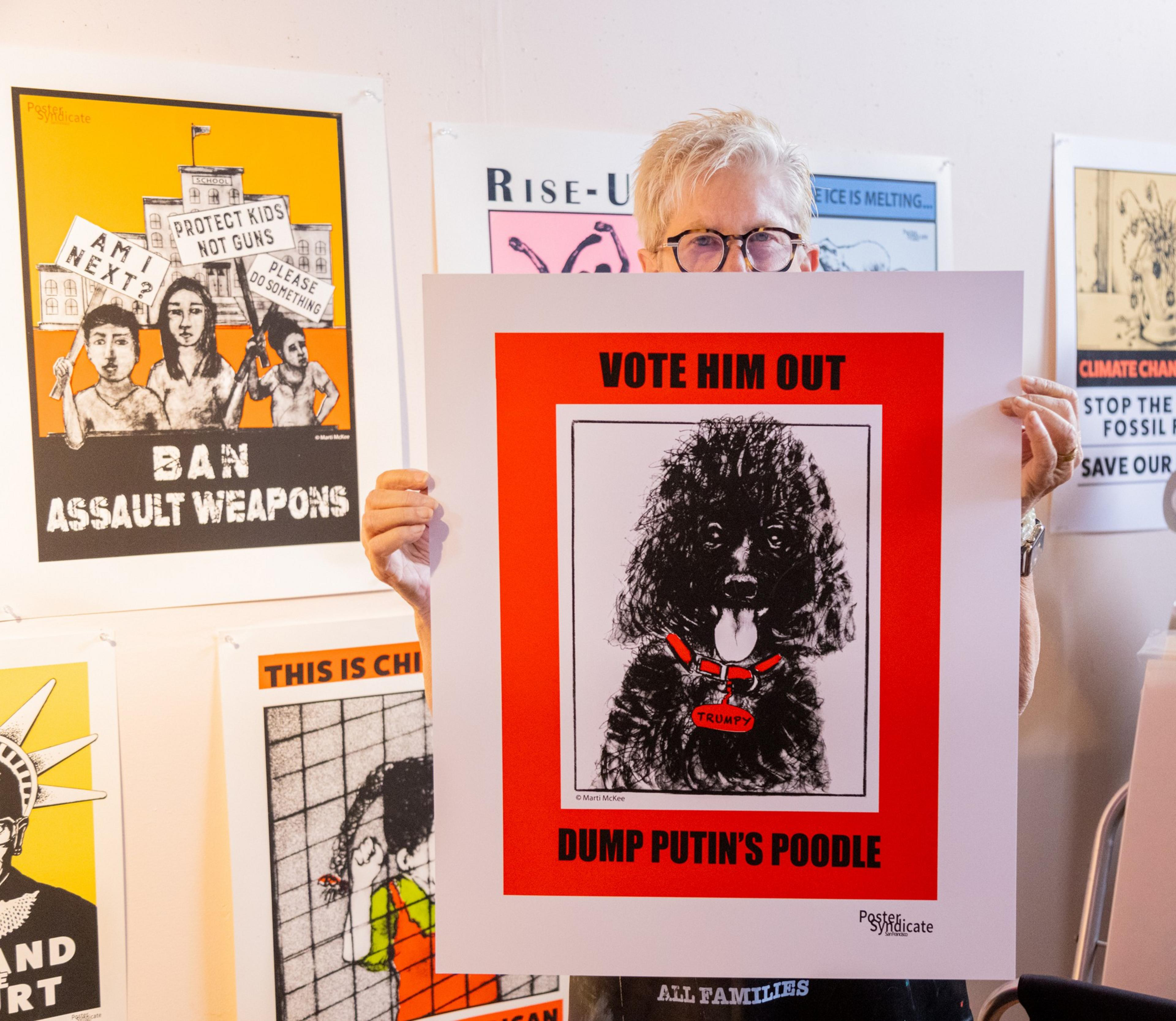 Person holds a sign with a dog and text &quot;VOTE HIM OUT - DUMP PUTIN'S POODLE&quot; among other political posters.