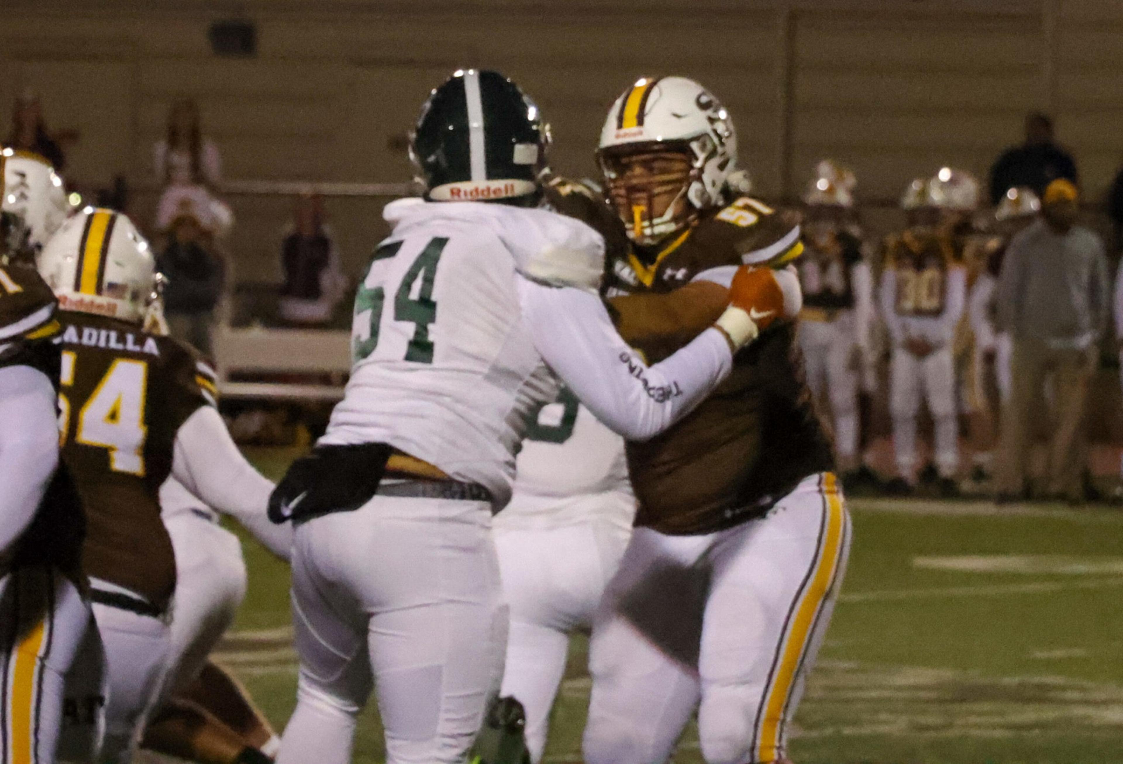 A football player in a white uniform with number 54 blocks a player in a brown uniform with yellow and white stripes during a nighttime game.