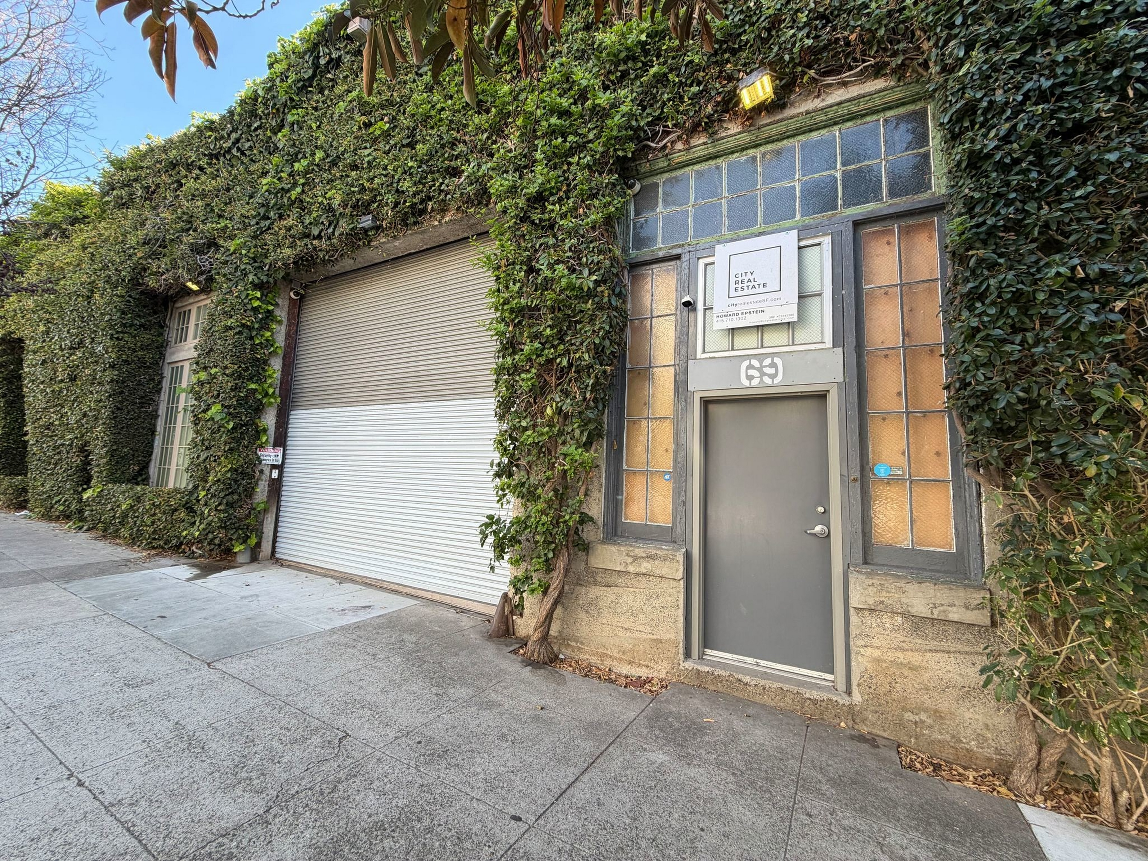 A gray door labeled "69" next to a large white roll-up garage door is framed by ivy-covered walls and frosted glass windows.