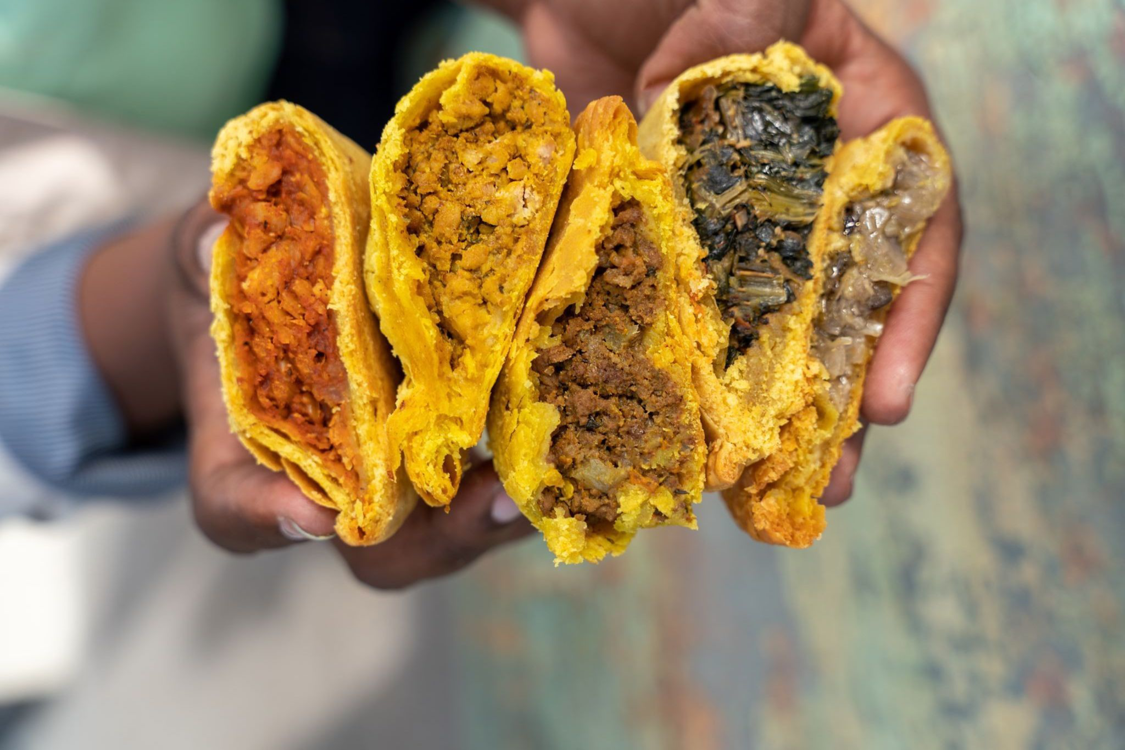 Five halves of stuffed, golden, fried dough pastries held in hands, each filled with different ingredients like meat, vegetables, or stewed fillings.