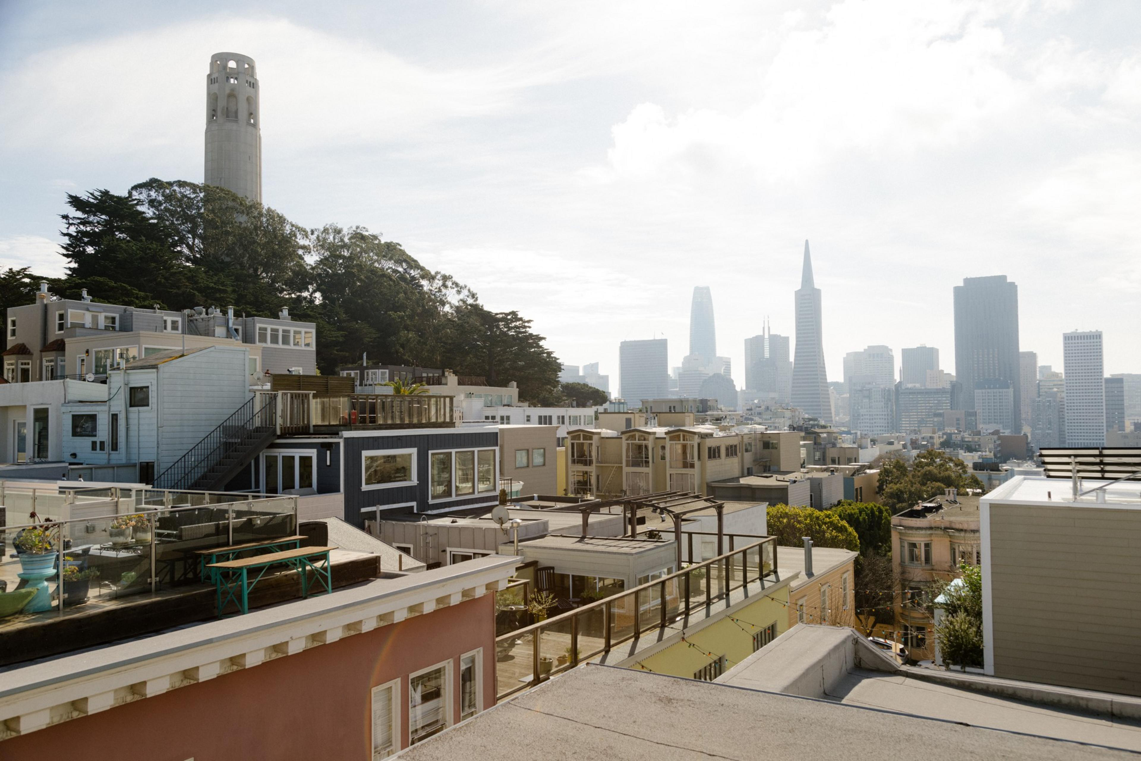 Cityscape with a tower on a hill, tiered buildings in the foreground, and skyscrapers in the distance under a clear sky.