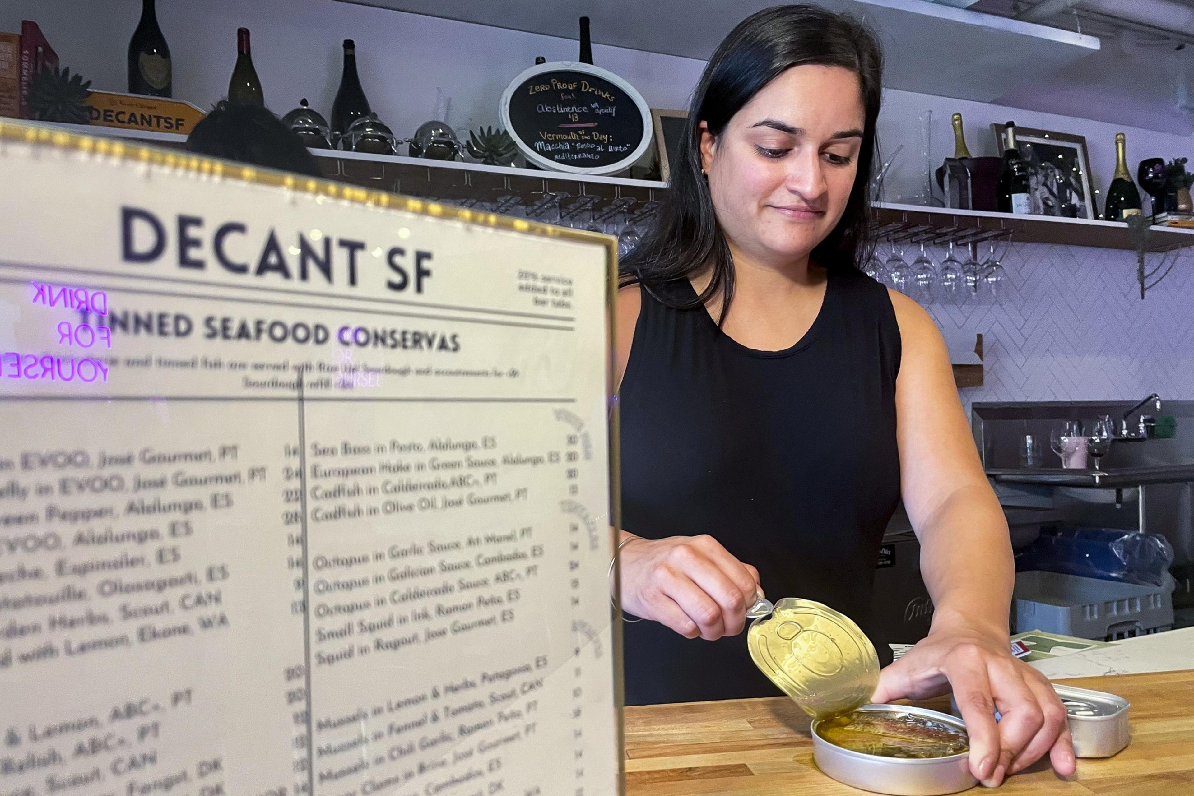 The owner of a small business peels back the lid on a can of fish.
