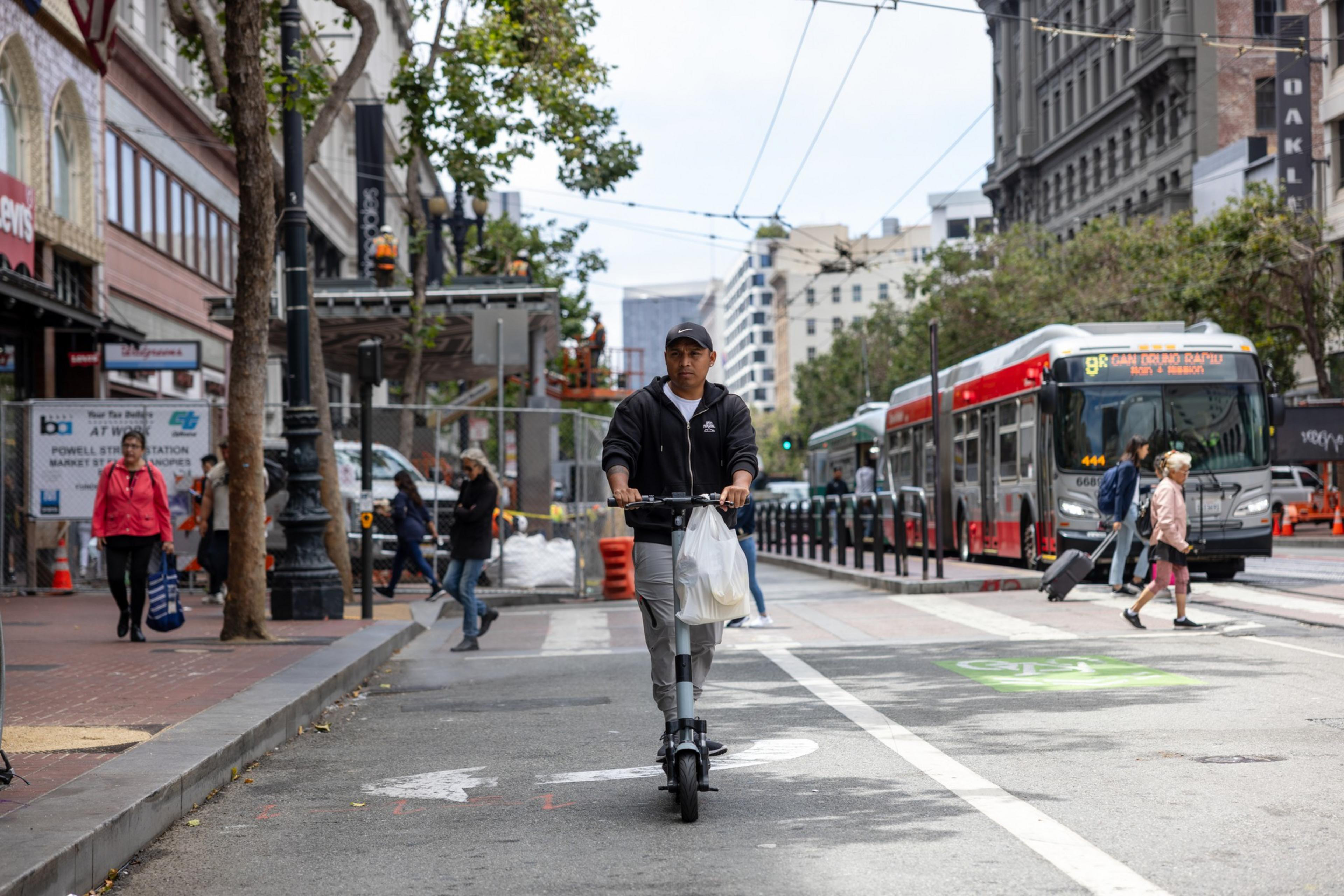A person on a scooter on Market Street with a bus and pedestrians in the background.