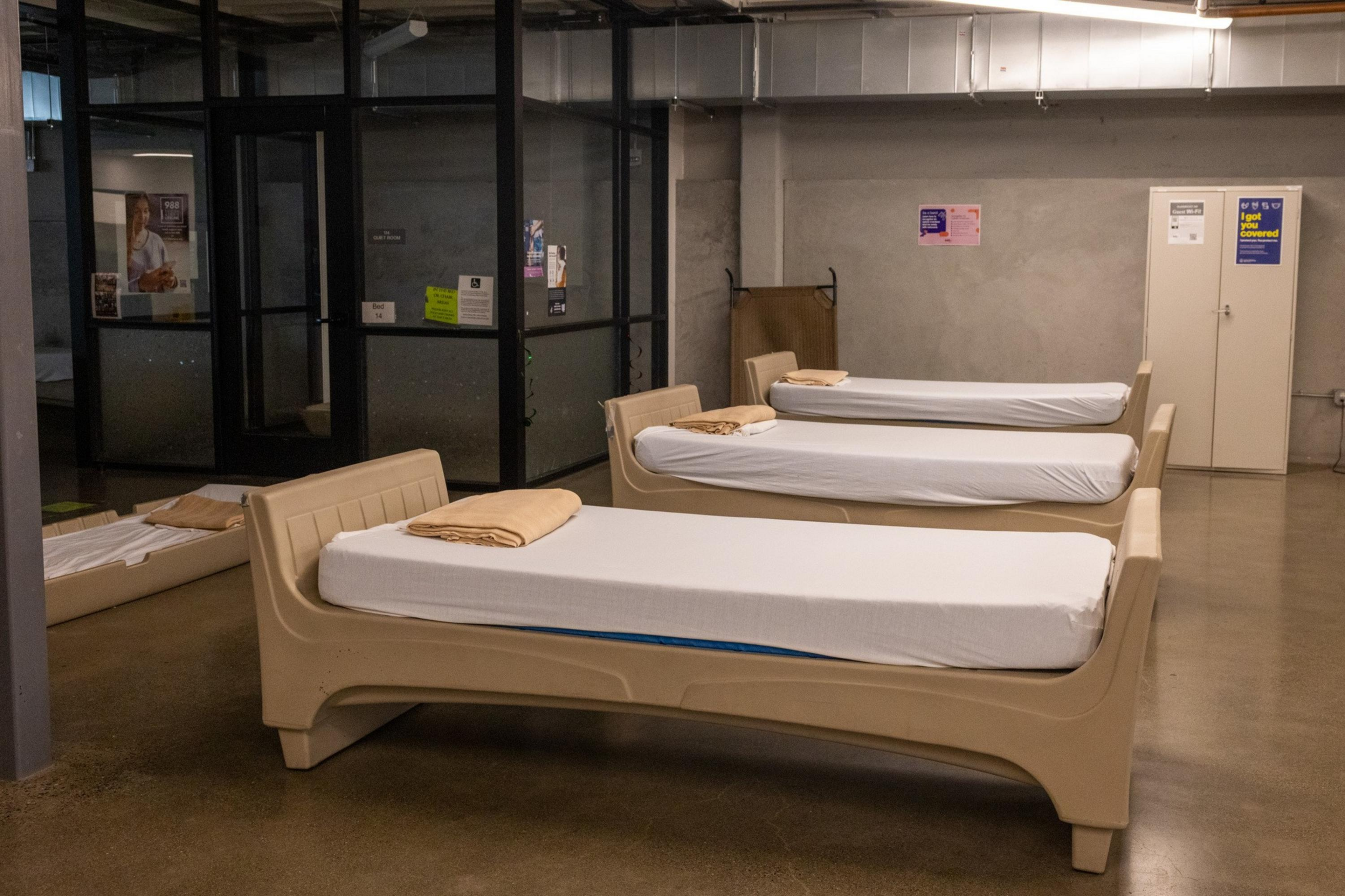 Three beige plastic beds with white sheets and folded tan blankets are ...