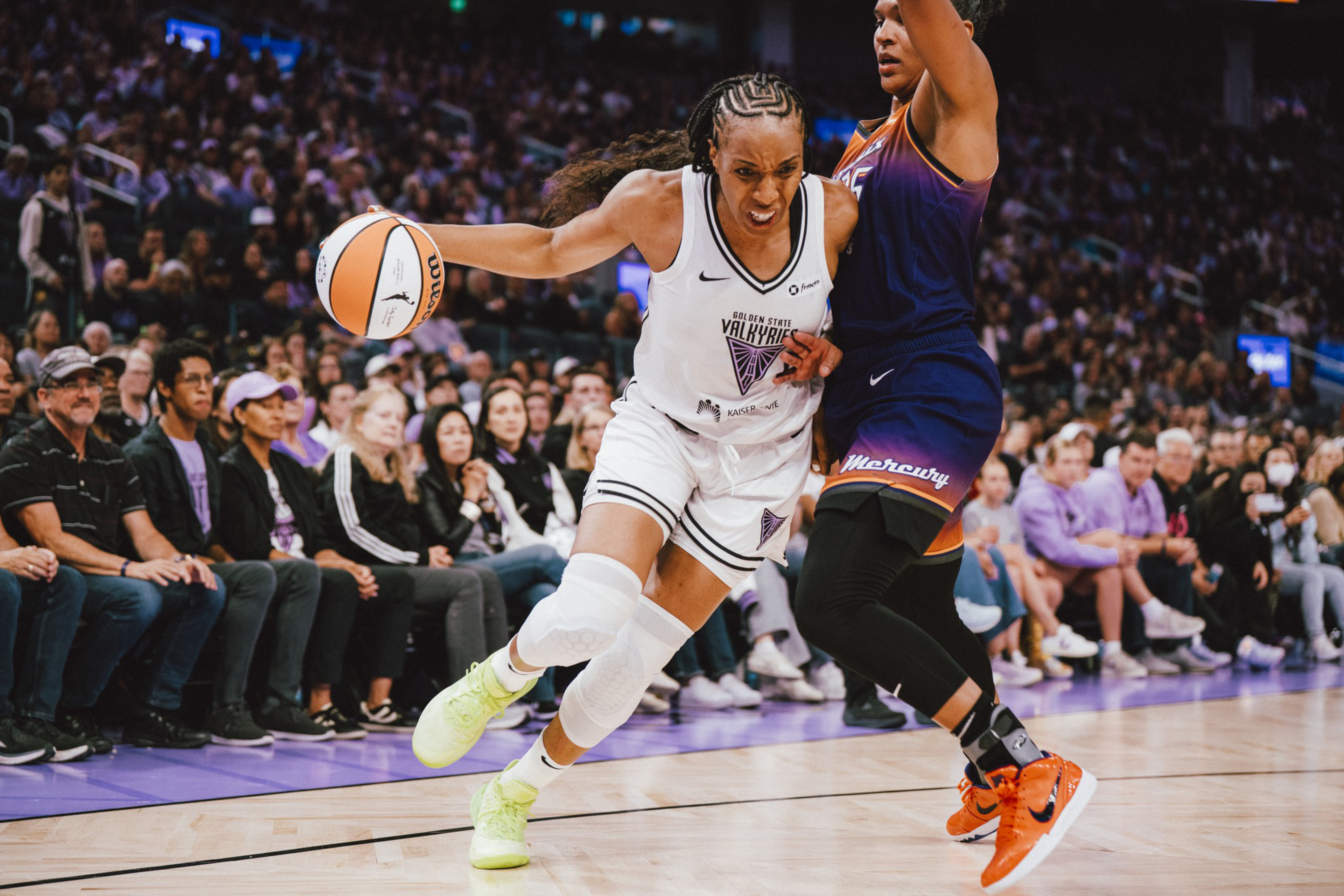 A basketball player in a white Oregon State Valkyries uniform drives past a defender in a dark Phoenix Mercury uniform during a packed game.