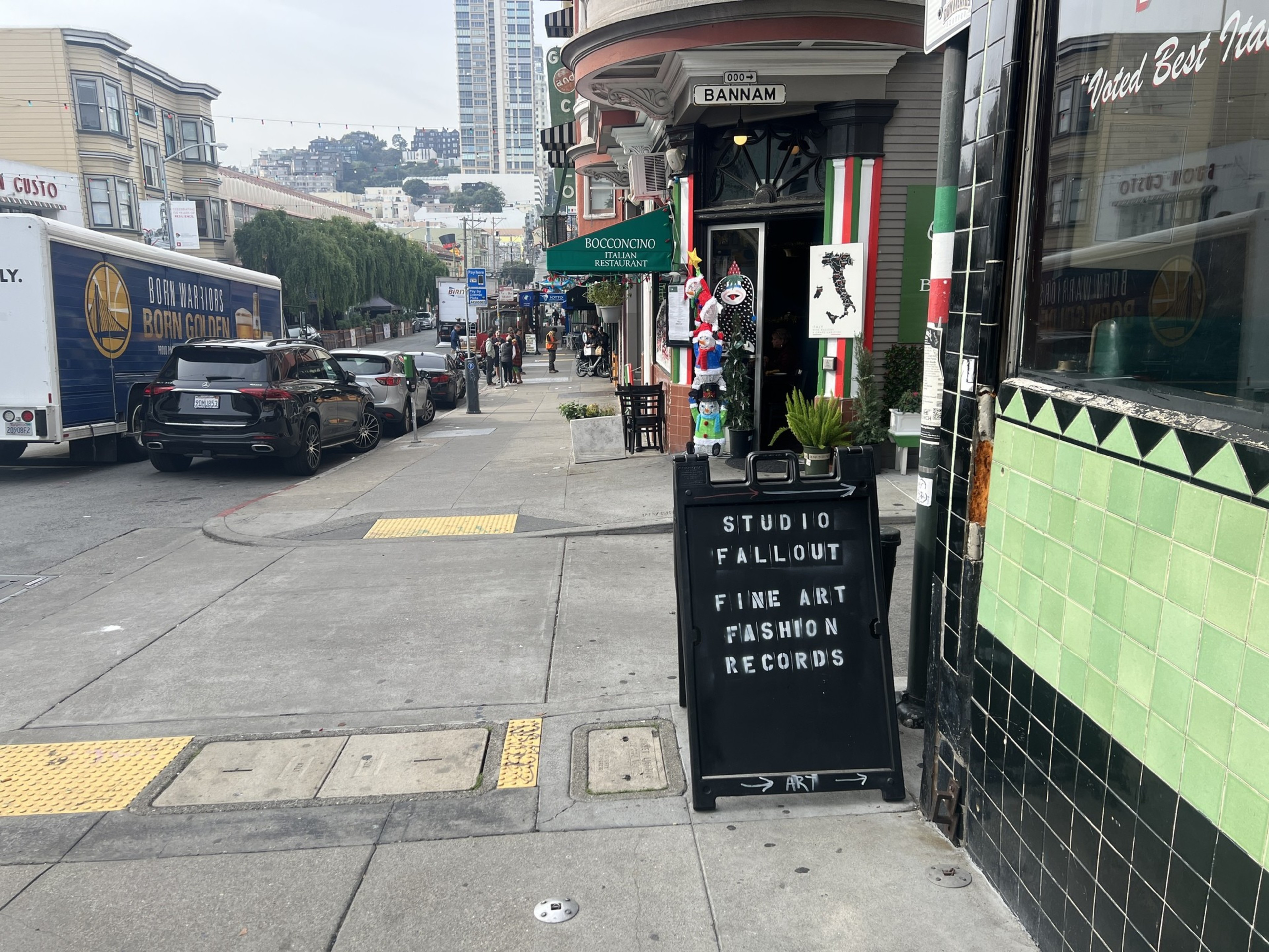 A black sandwich style sign on a sidewalk says Studio Fallout, Fine Art, Fashion, Records.