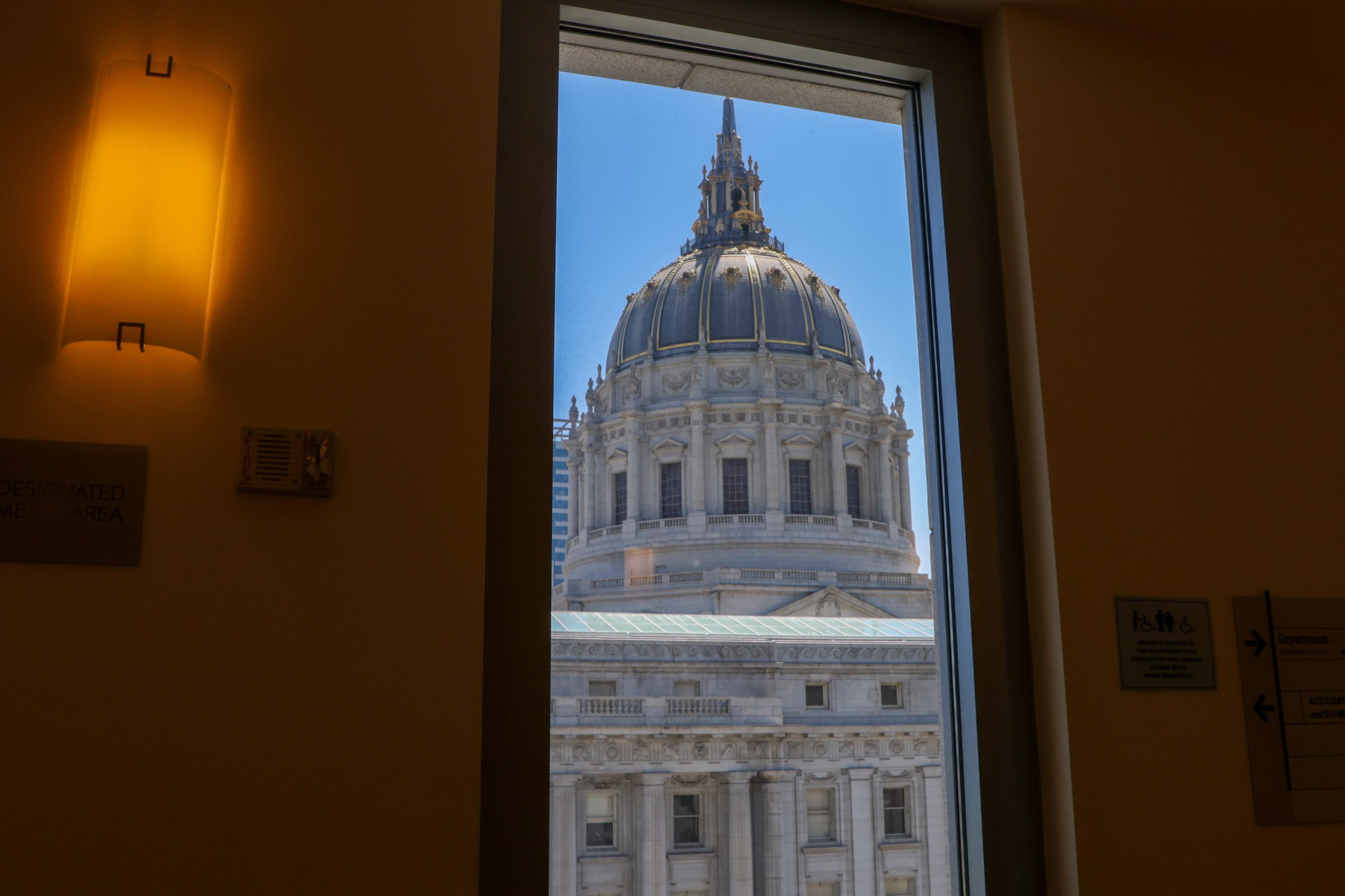 A large, ornate gray dome with a spire is viewed through a rectangular window from inside a dimly lit room.