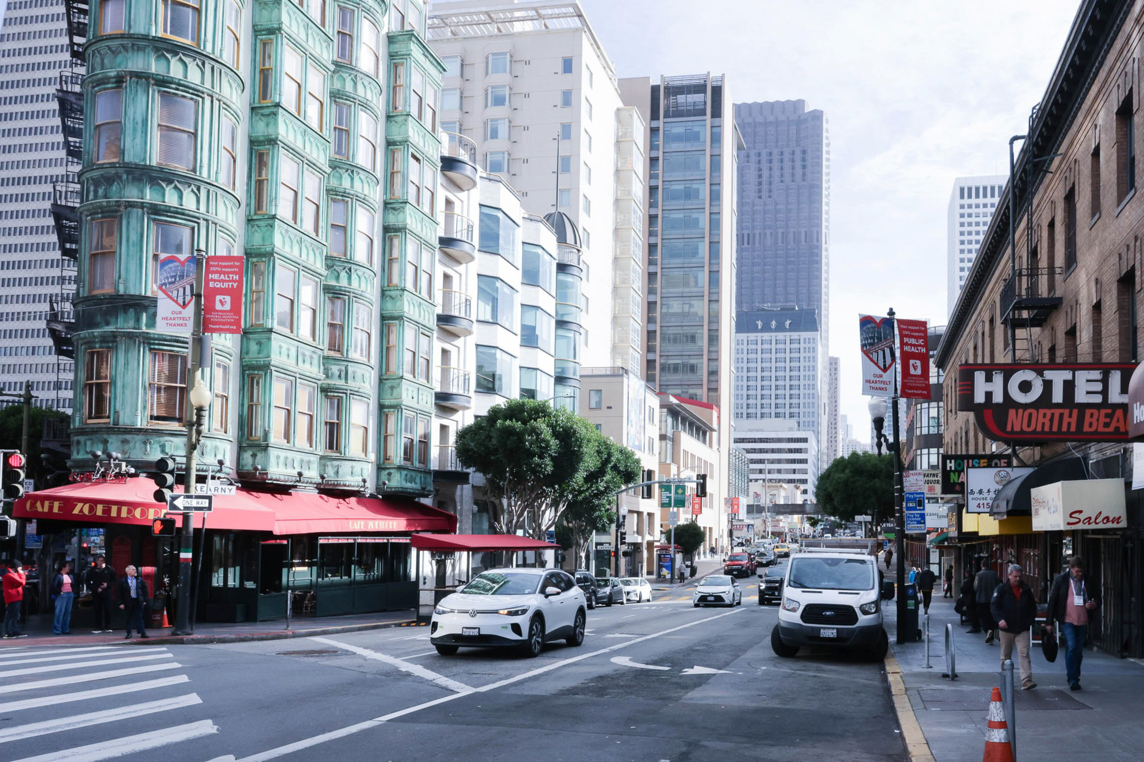A bustling city street with historic and modern buildings, pedestrians, and vehicles under a clear sky.