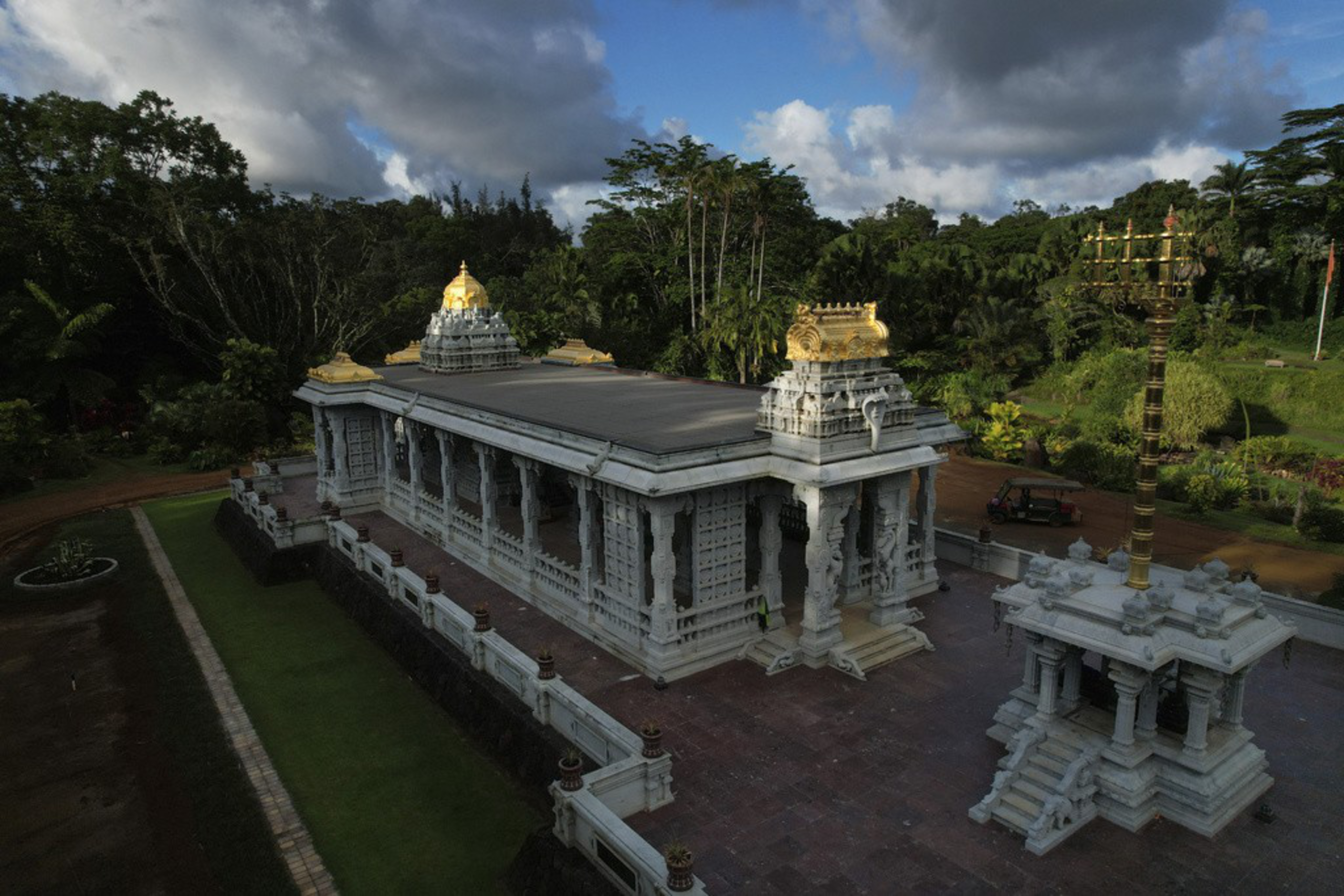 A white temple made of granite and topped with gold decorations sits in a tropical clearing.