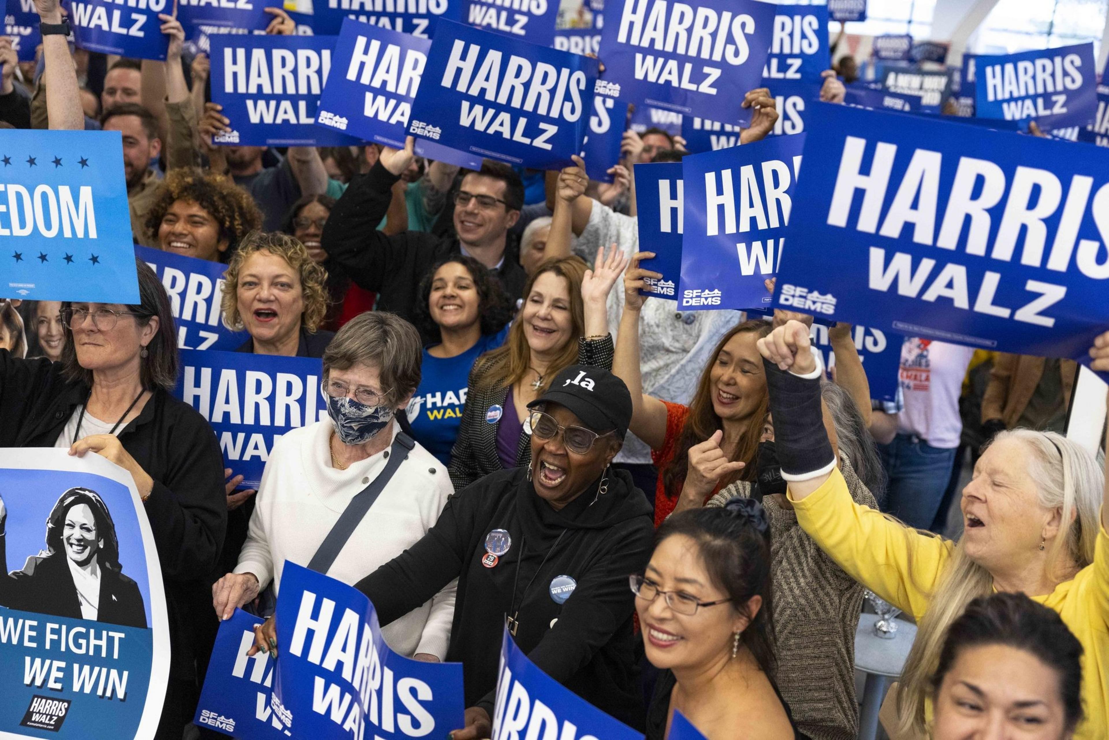 A joyous, diverse crowd holds "Harris Walz" signs, some yelling, promoting unity and support at what appears to be a political rally.