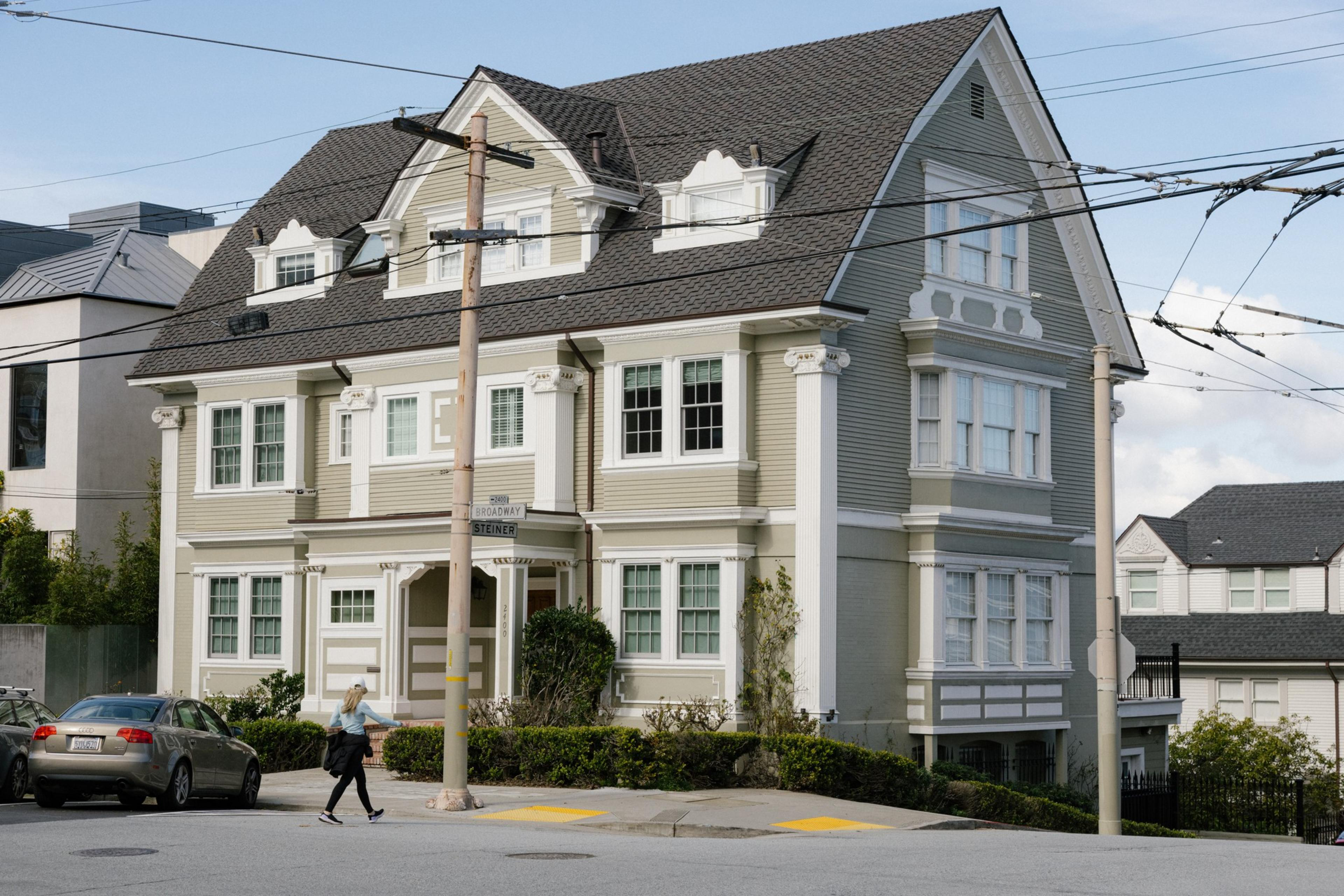 A large, traditional house with a gabled roof and a street corner with a pedestrian walking by.
