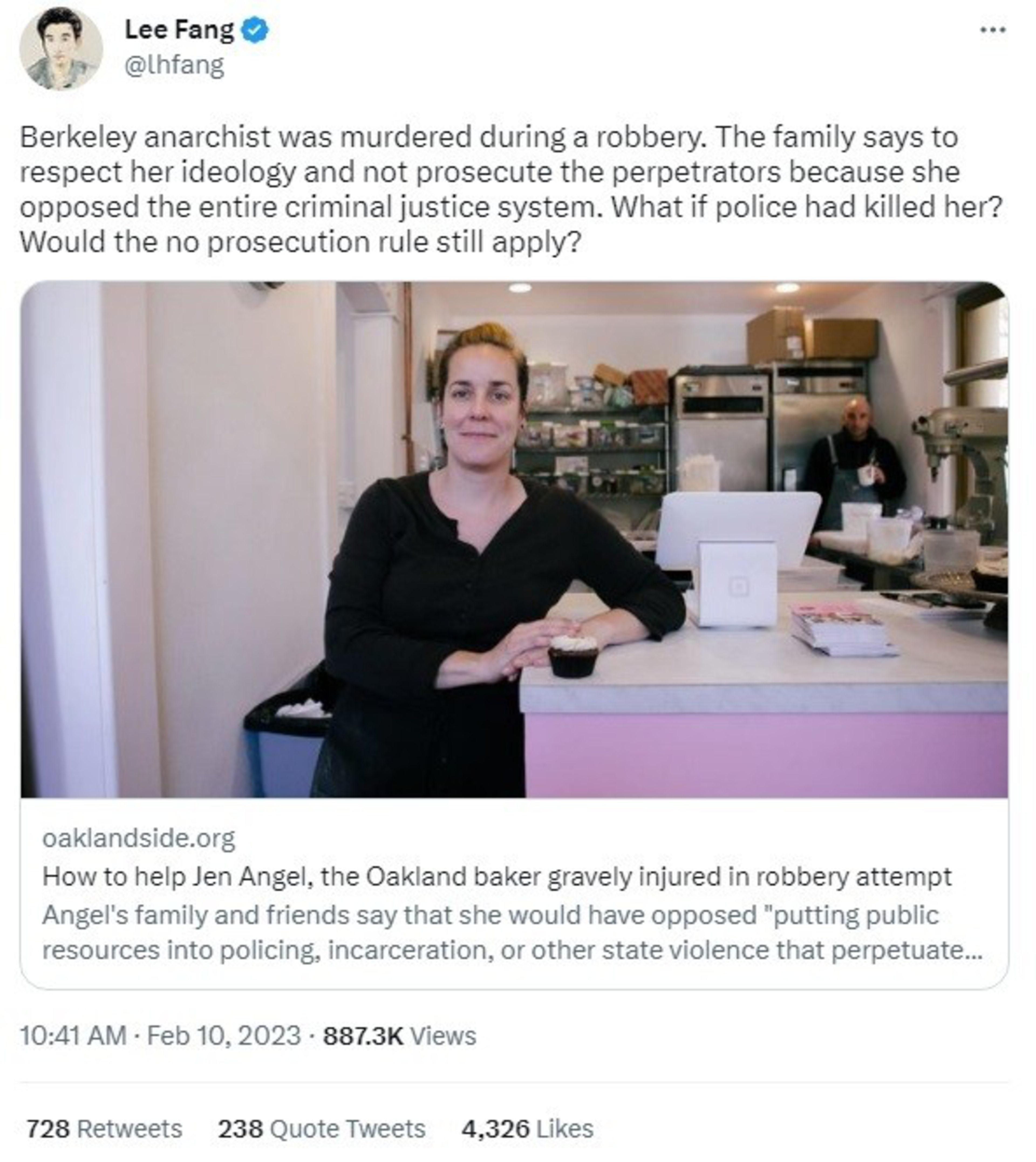 A woman in a black shirt stands behind a counter in a bakery, holding a cupcake, with kitchen equipment and a man in the background.