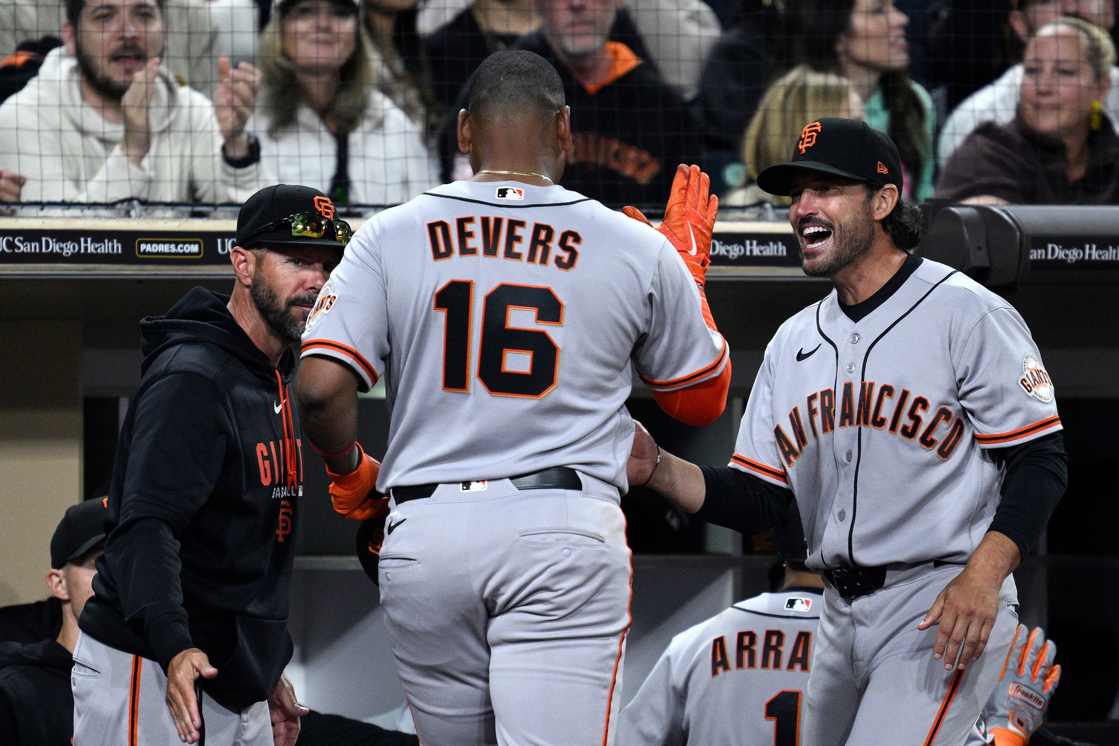 A baseball player wearing jersey number 16 labeled “Devers” is high-fiving teammates in San Francisco Giants uniforms in the dugout.