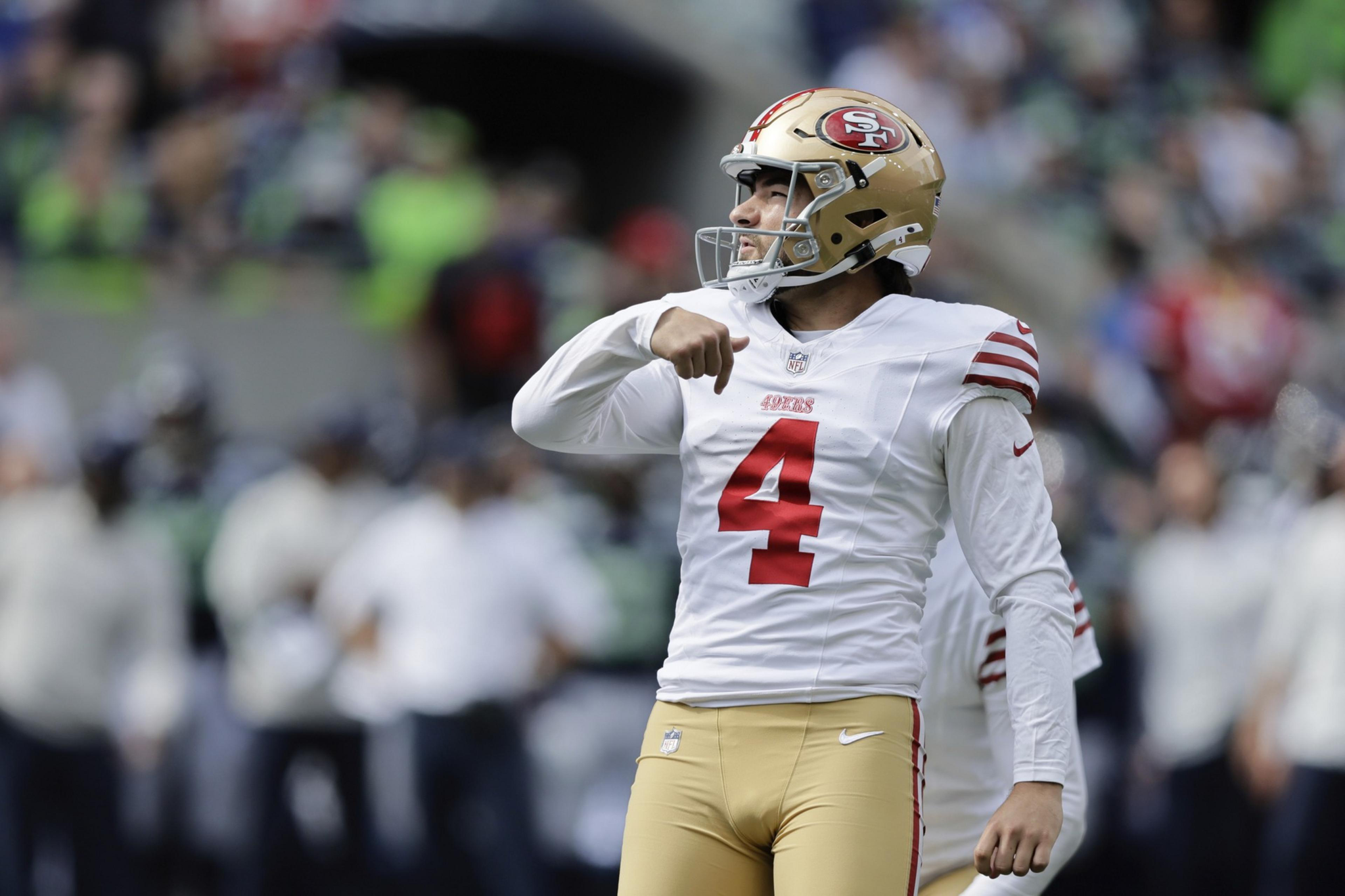 A San Francisco 49ers player wearing a white jersey with number 4 and gold helmet celebrates on the field with a crowd blurred in the background.