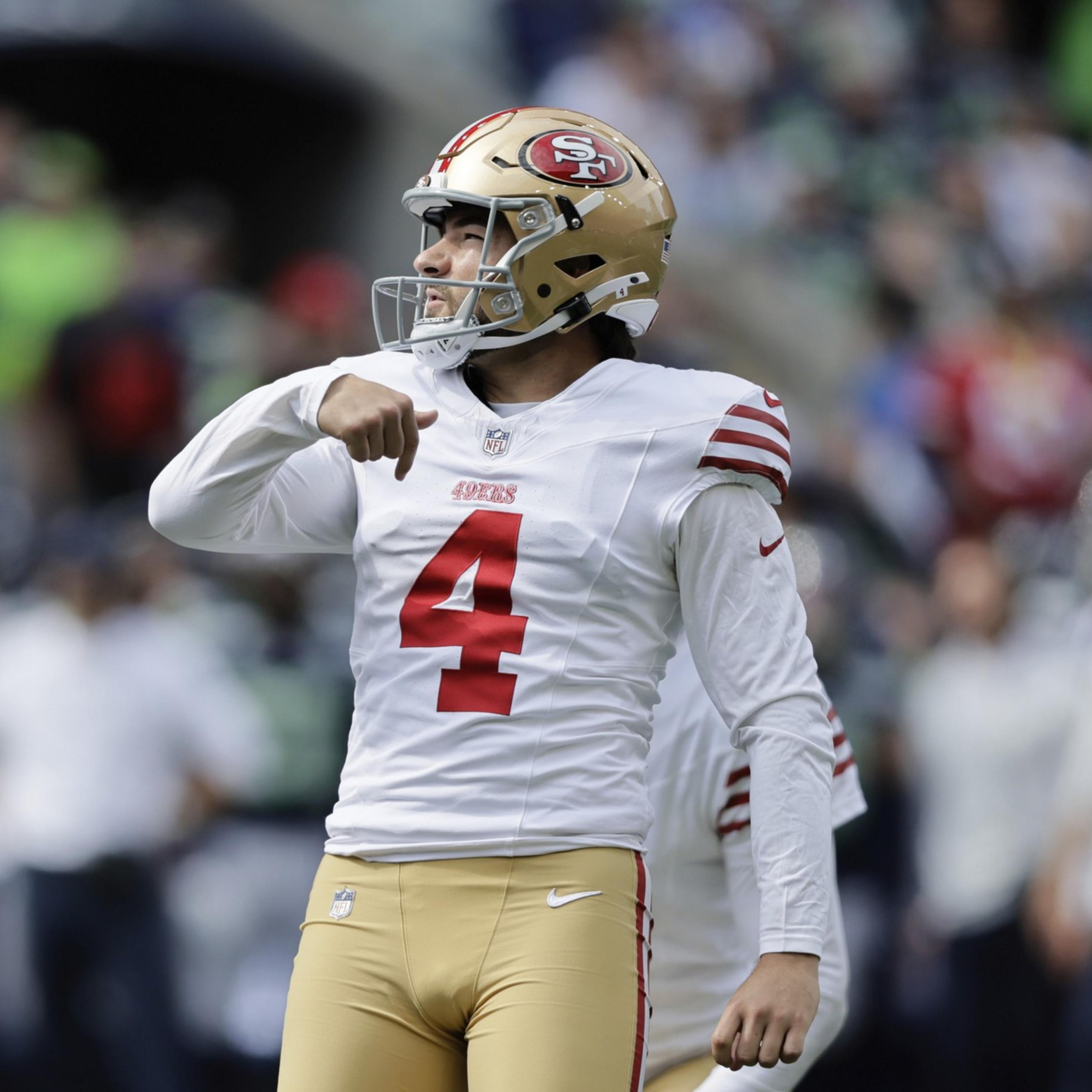 A San Francisco 49ers player wearing a white jersey with number 4 and gold helmet celebrates on the field with a crowd blurred in the background.