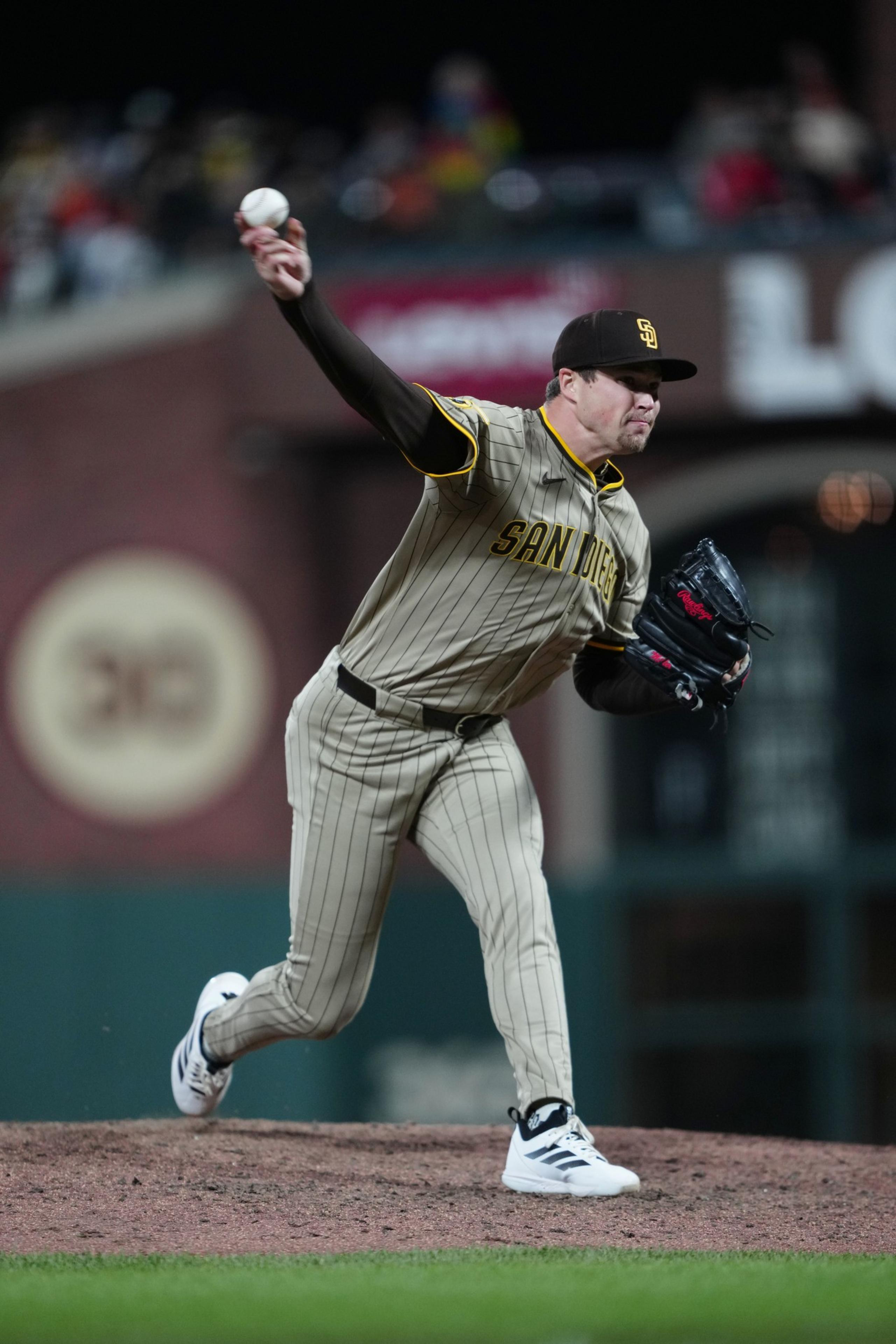 A baseball pitcher in a San Diego uniform throws a pitch on the mound during a night game.