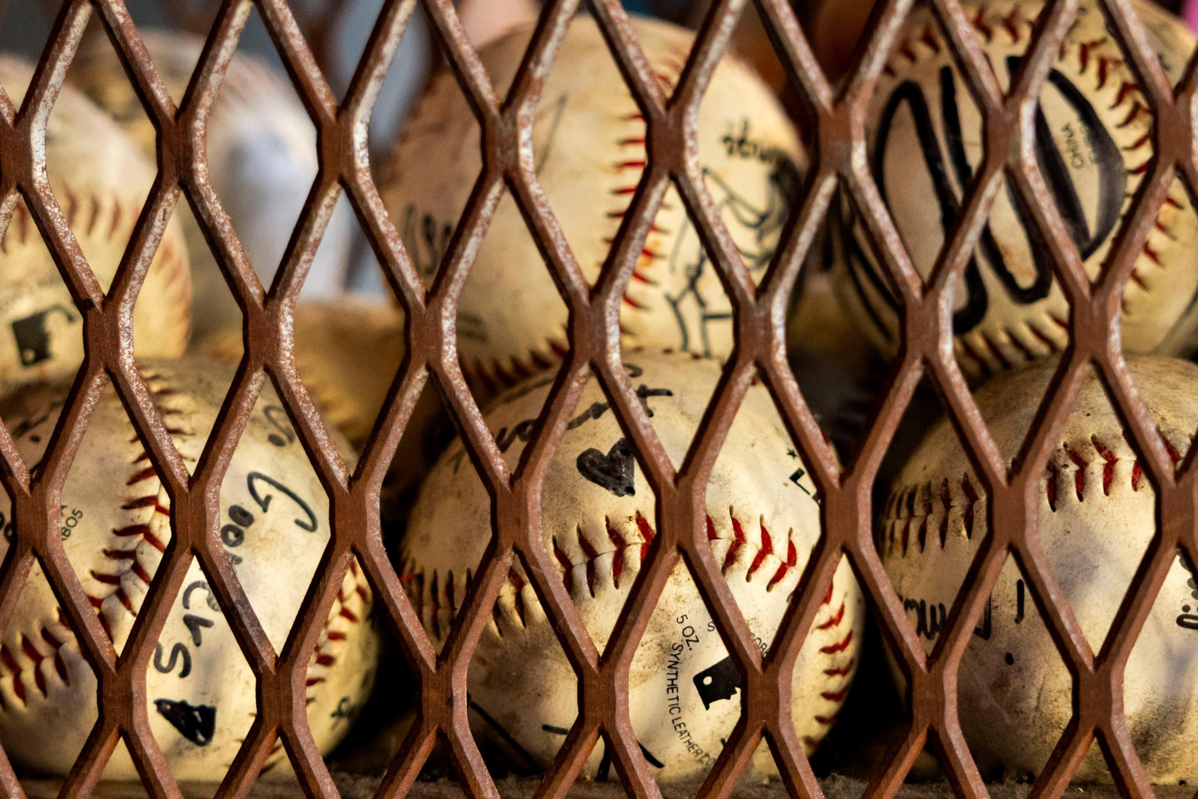 A collection of signed, worn baseballs is held behind a rusted metal mesh fence or grate.