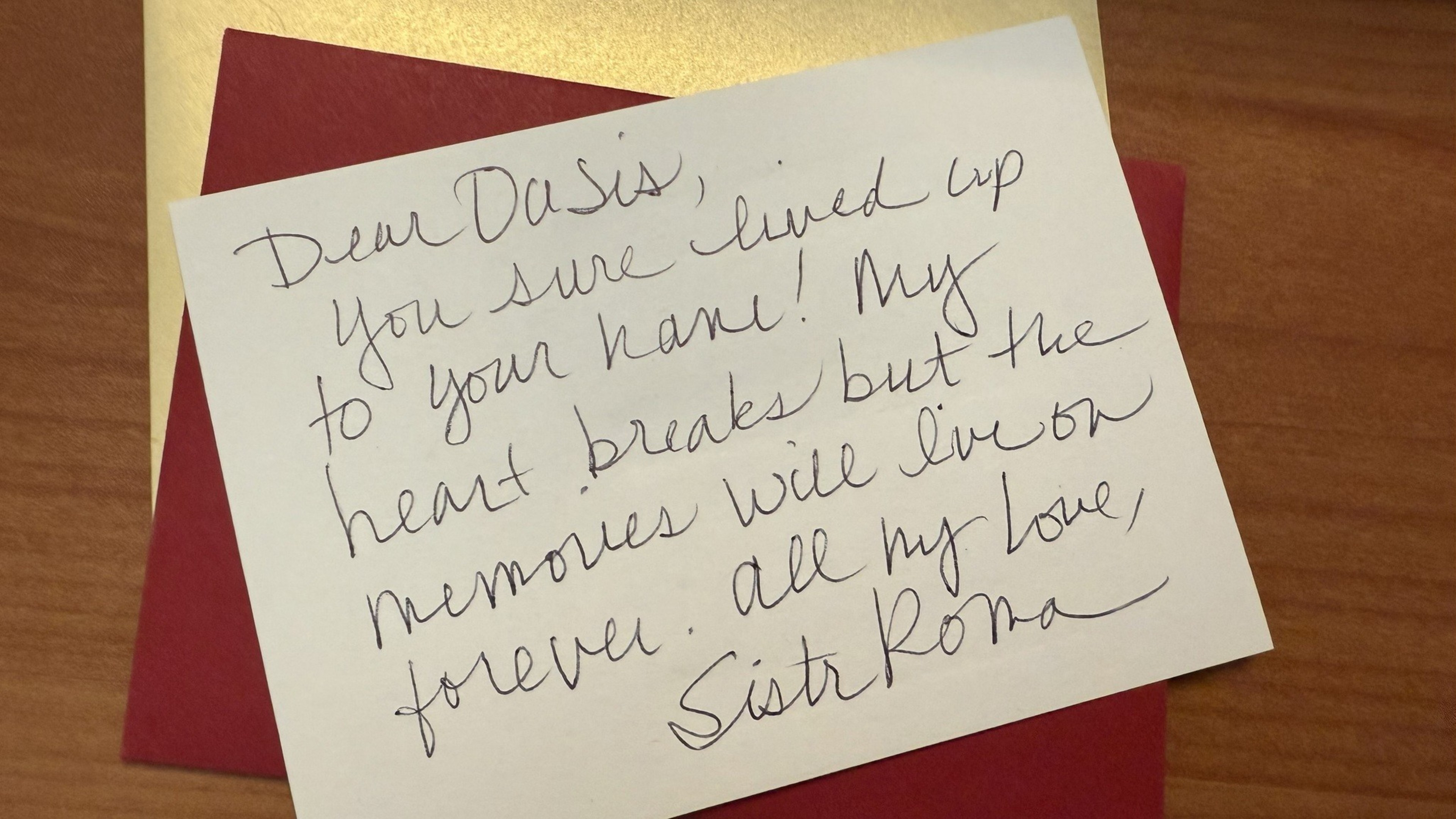 A handwritten note on a white card, placed on a red envelope, expresses sympathy and love, signed "Sister Roma."