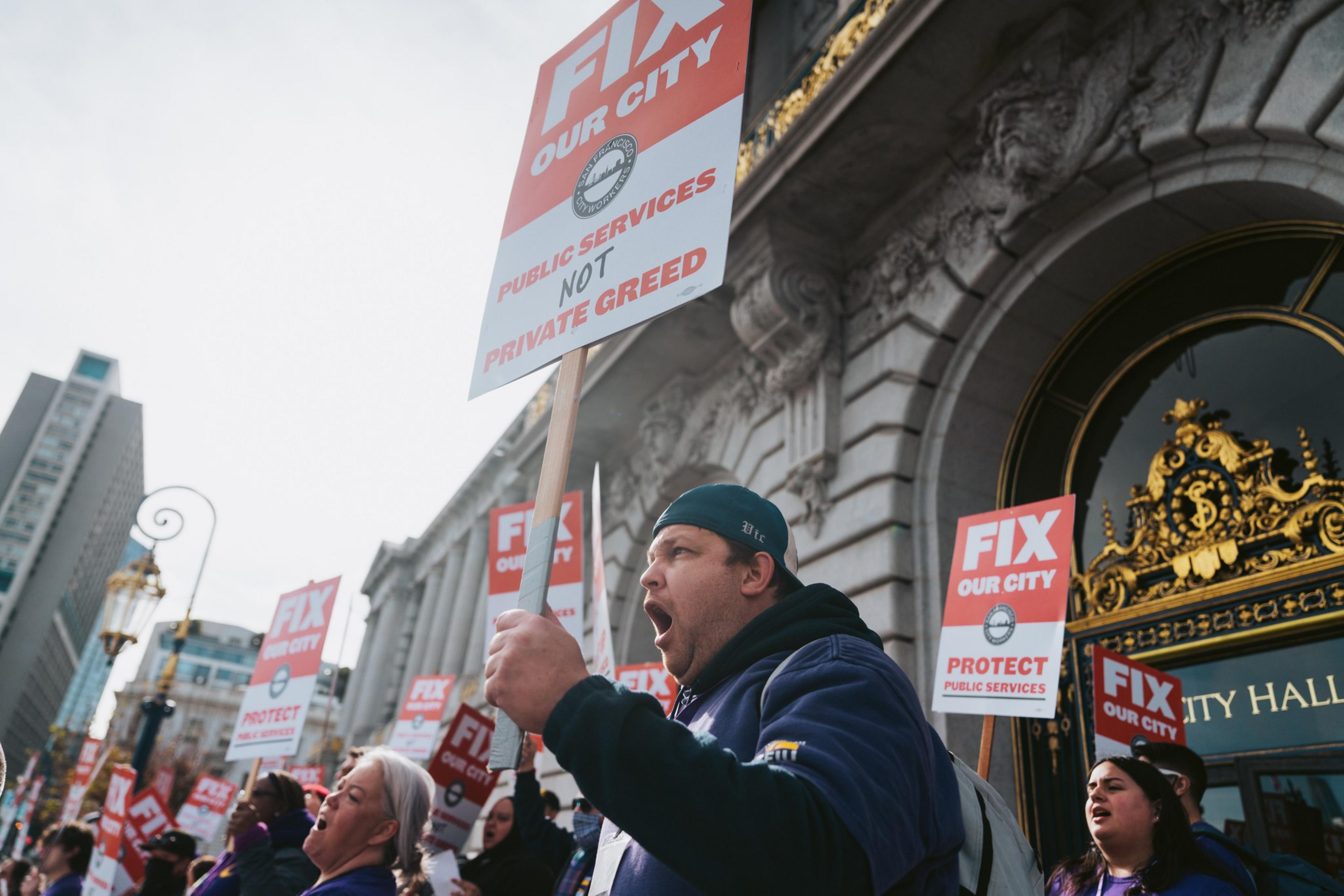 A group is protesting with signs reading "FIX OUR CITY" in front of City Hall.