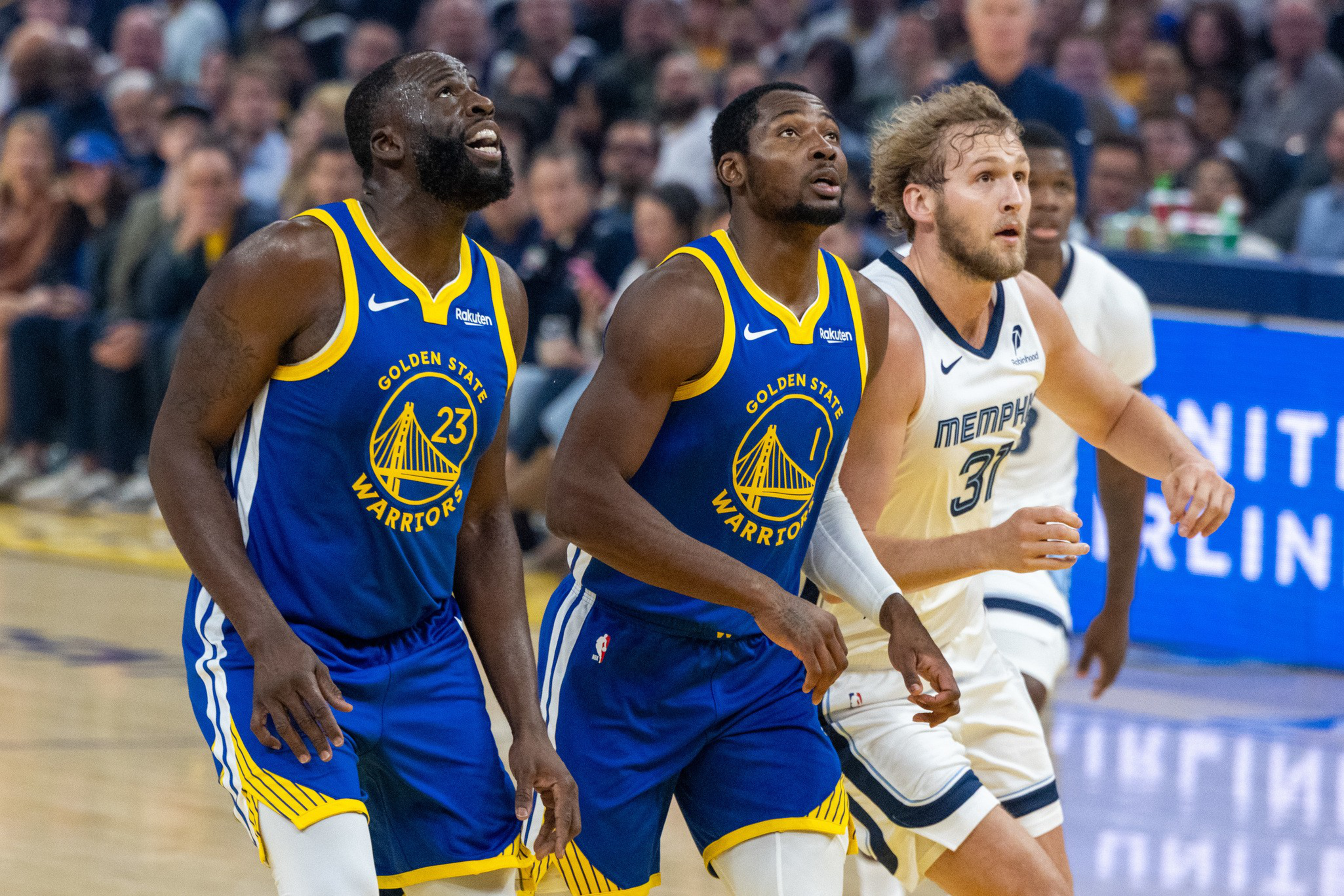 Two Golden State Warriors players and a Memphis Grizzlies player closely watch the basketball during a game, anticipating the next play.
