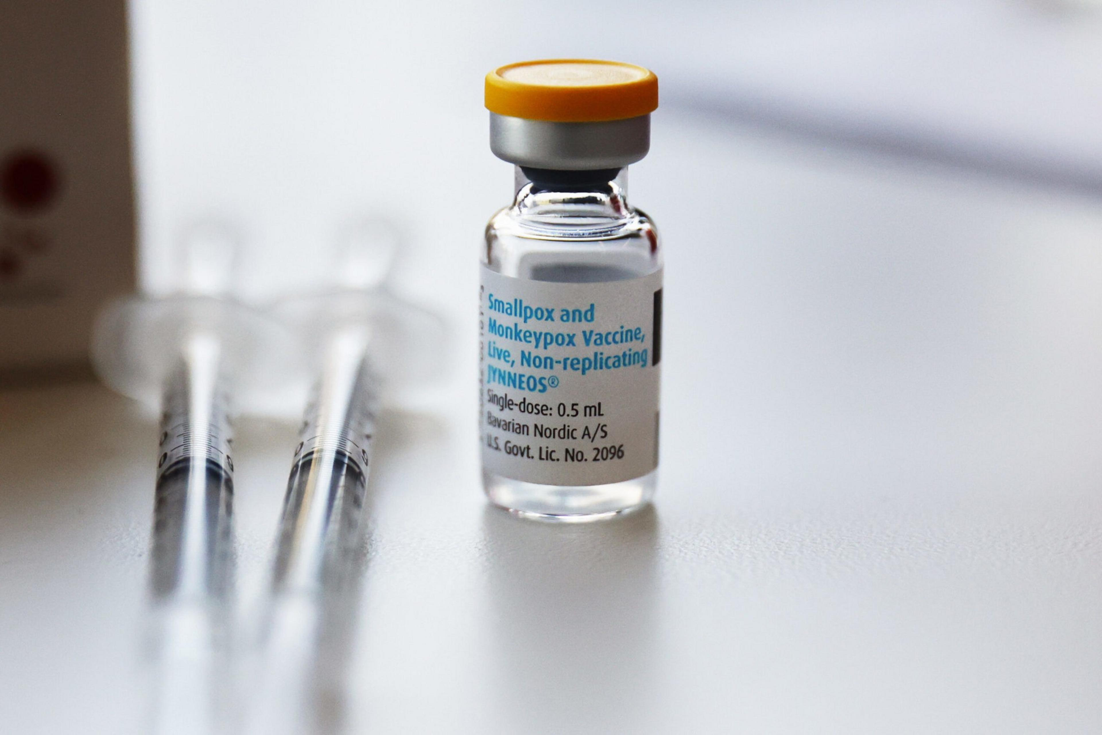 A vial labeled "Smallpox and Monkeypox Vaccine, live, Non-replicating" sits next to two syringes on a white surface.