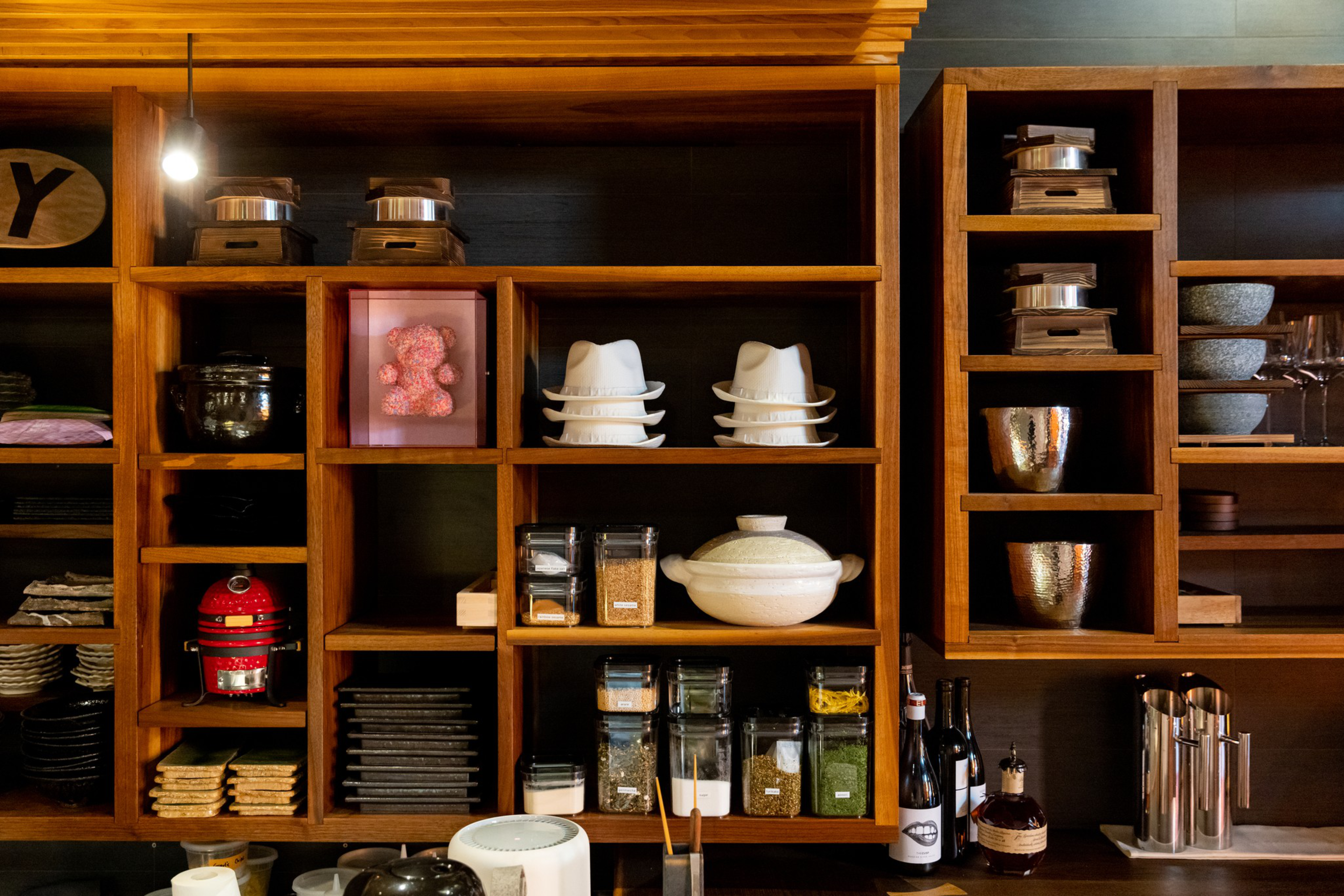 Wooden shelves hold kitchen items including stacked white bowls, glass jars with spices, wine bottles, metal containers, and a red stand mixer.