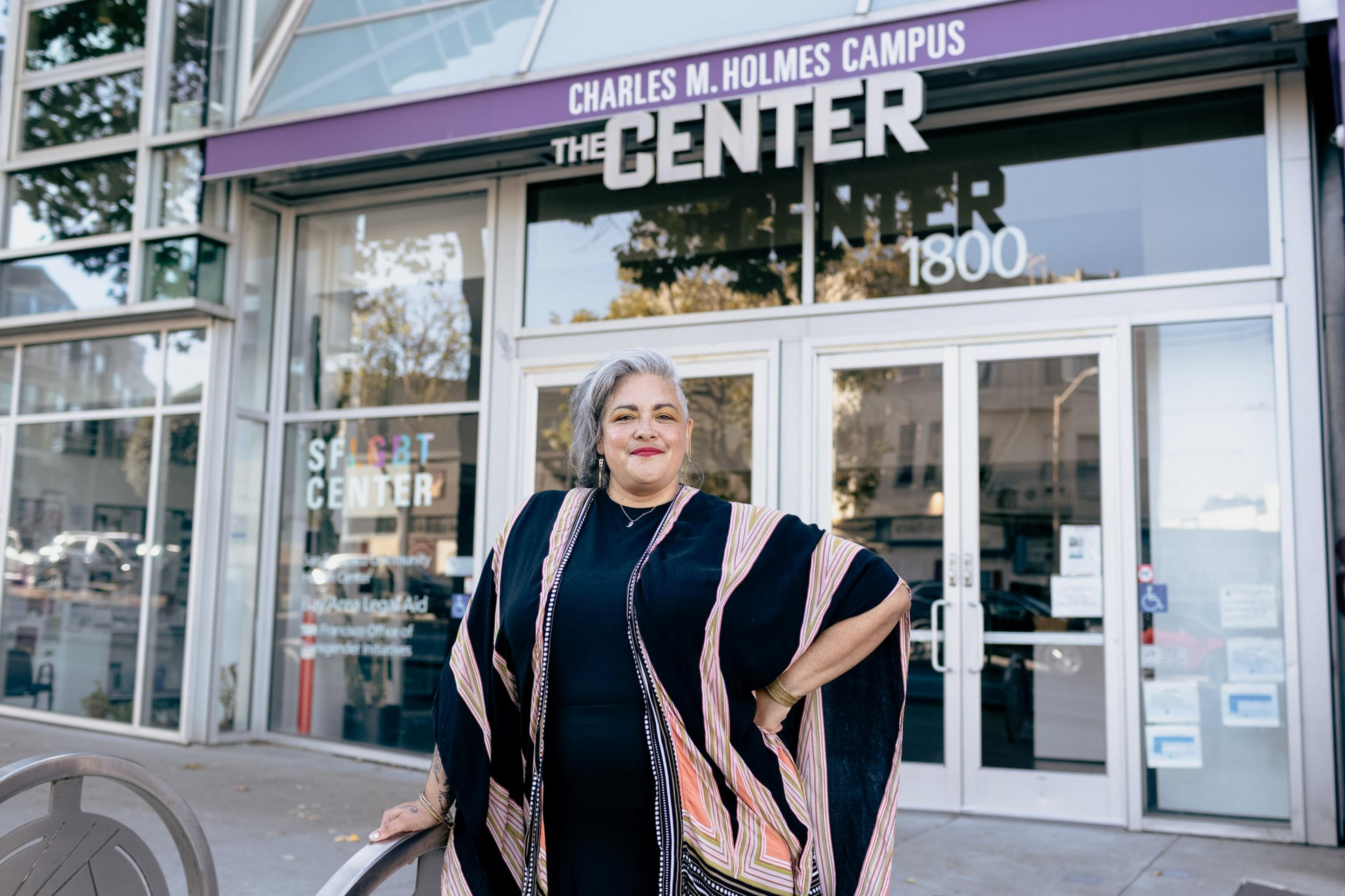 A confident woman stands with one hand on a chair and the other on her hip outside a building labeled "Charles M. Holmes Campus, The Center, 1800."