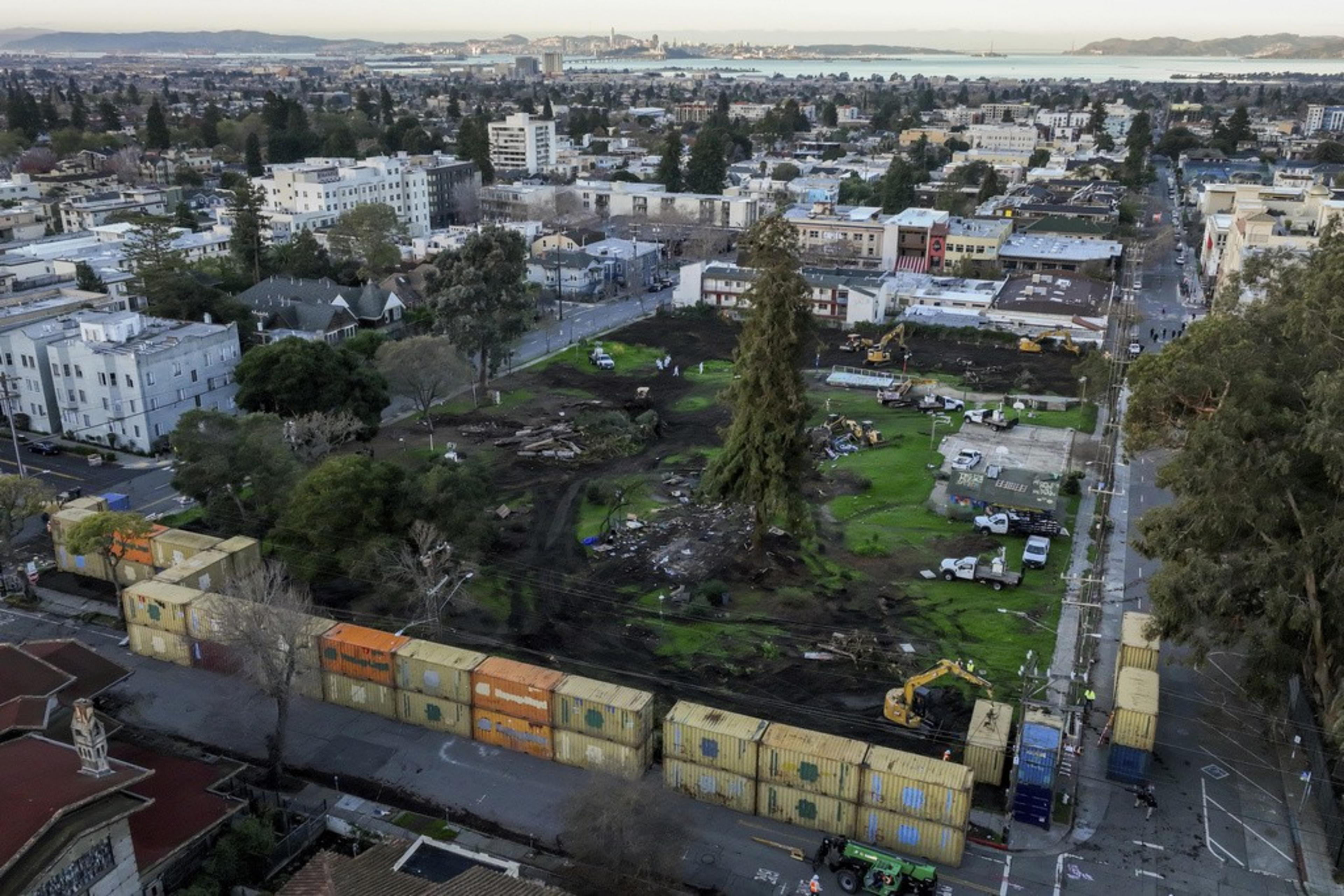 Aerial view of an urban area with a park, construction machinery, cargo containers, and city backdrop.