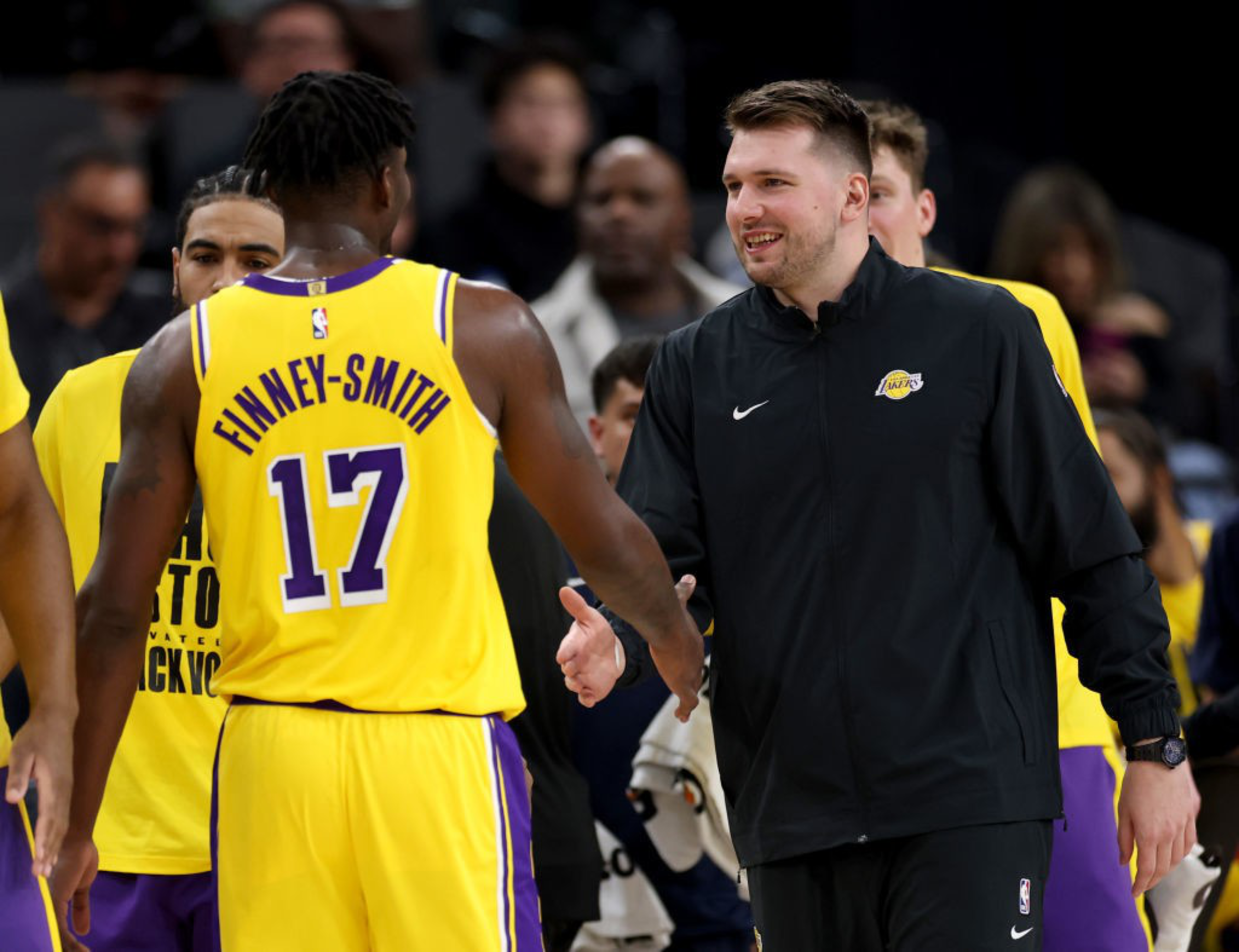 A basketball player in a yellow jersey with &quot;Finney-Smith 17&quot; greets a man in a black Nike jacket. They are smiling, amidst other people dressed similarly.