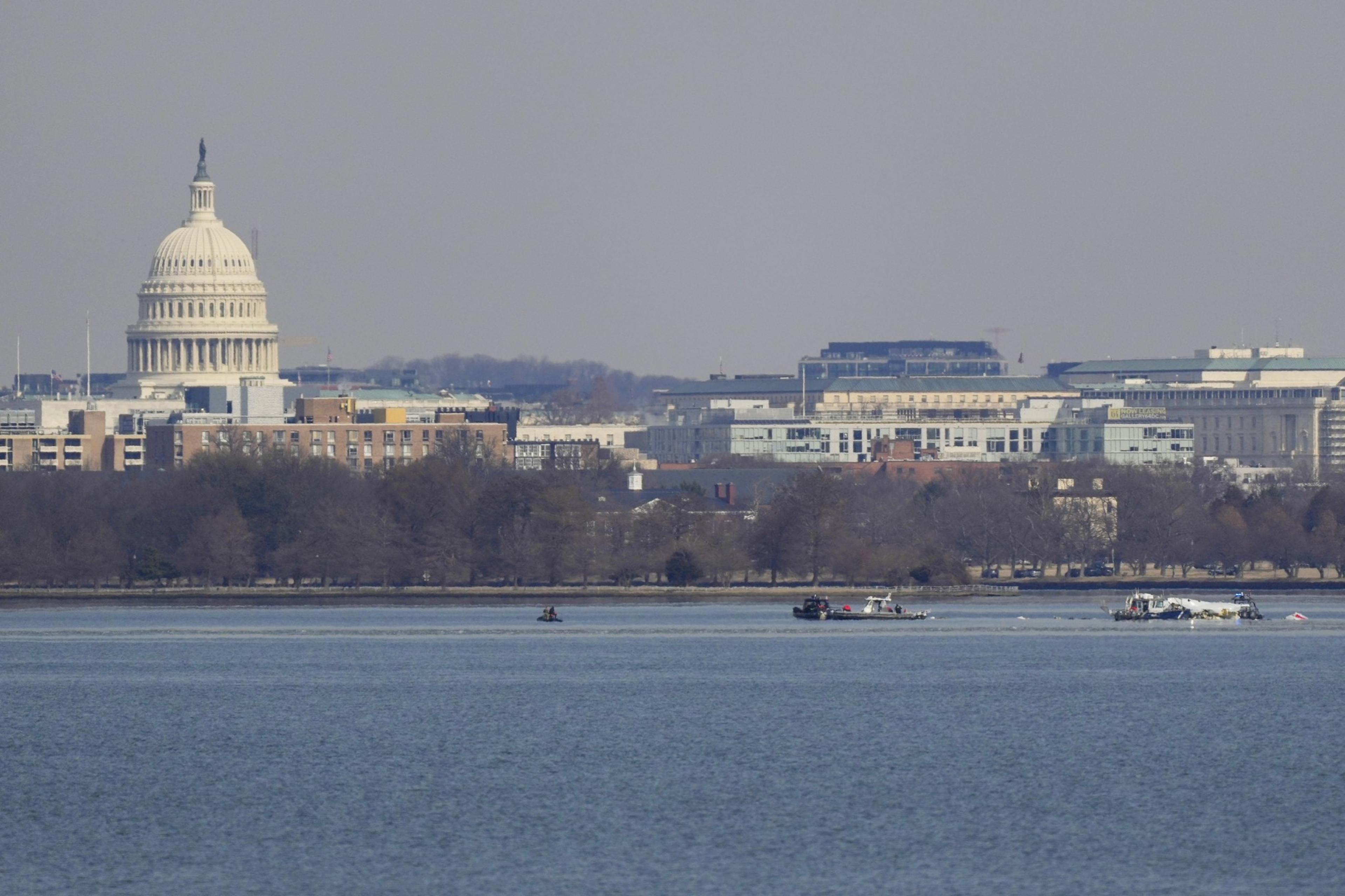In the image, the U.S. Capitol building stands prominently, framed by urban buildings and trees in front, with a calm body of water in the foreground.