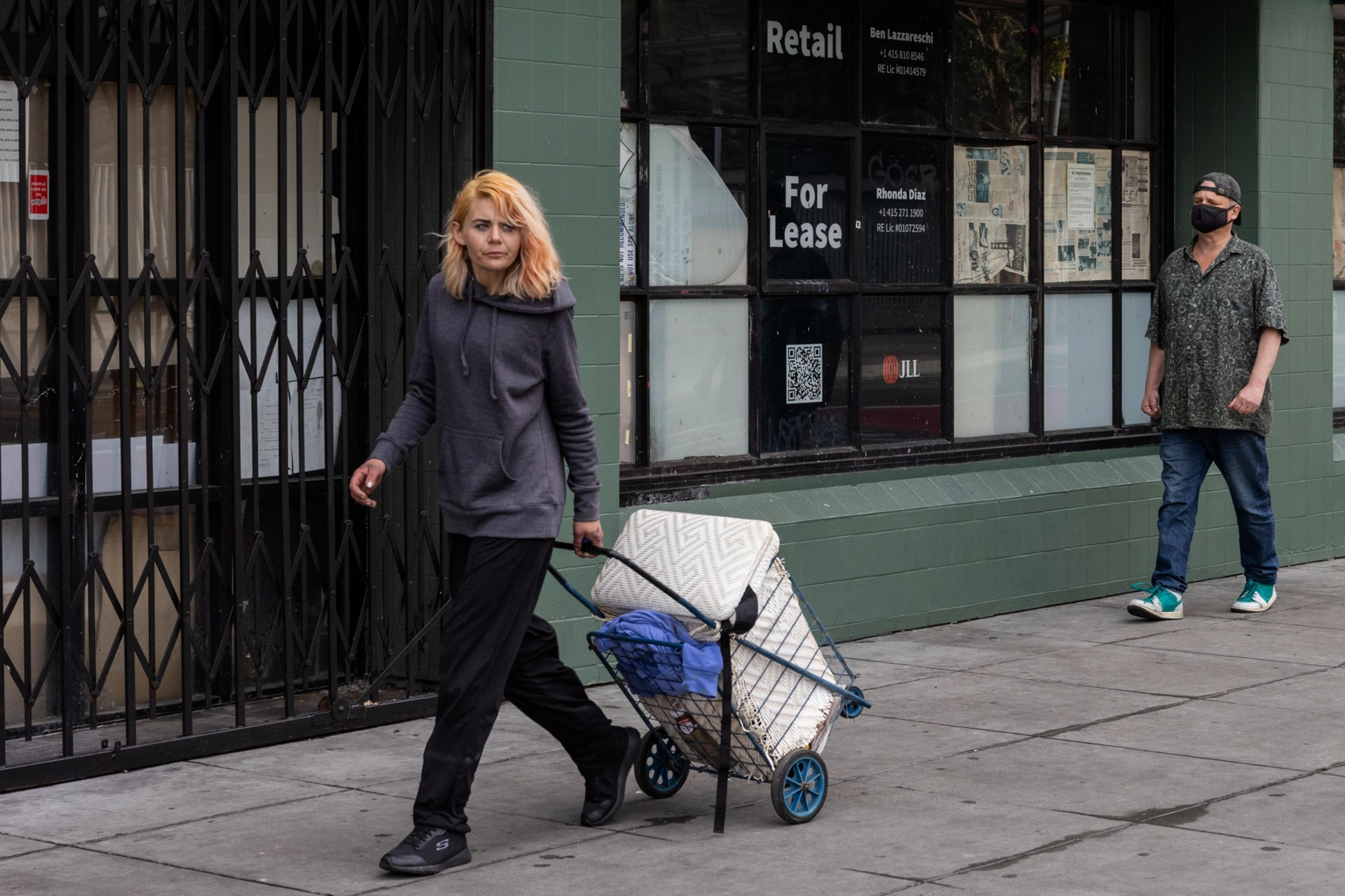 Two people walk down a city street next to a building with signage that reads "For Lease".